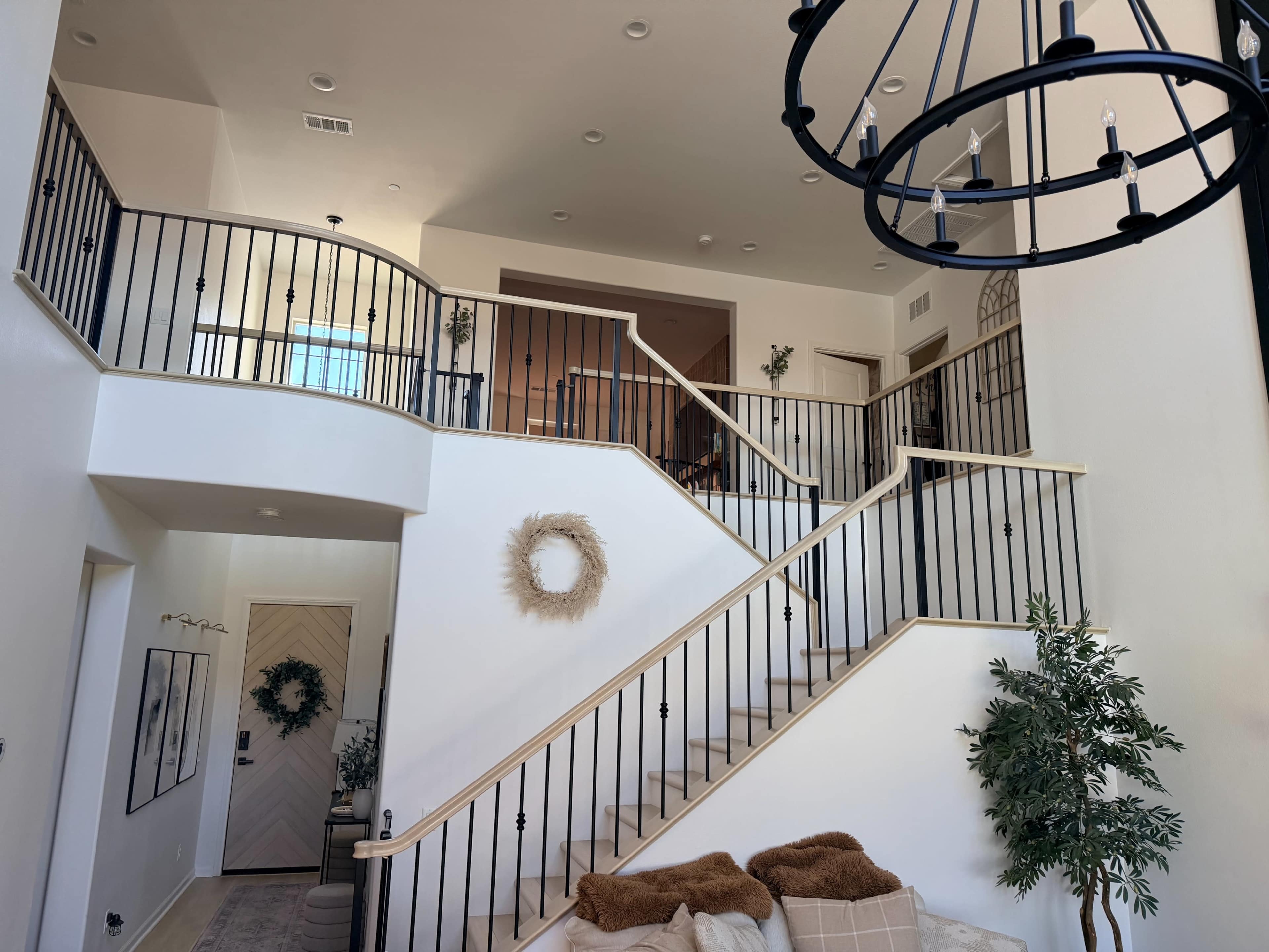 The image shows a two-story foyer with a curved staircase and decorative railings, accompanied by a chandelier and a cozy seating area.