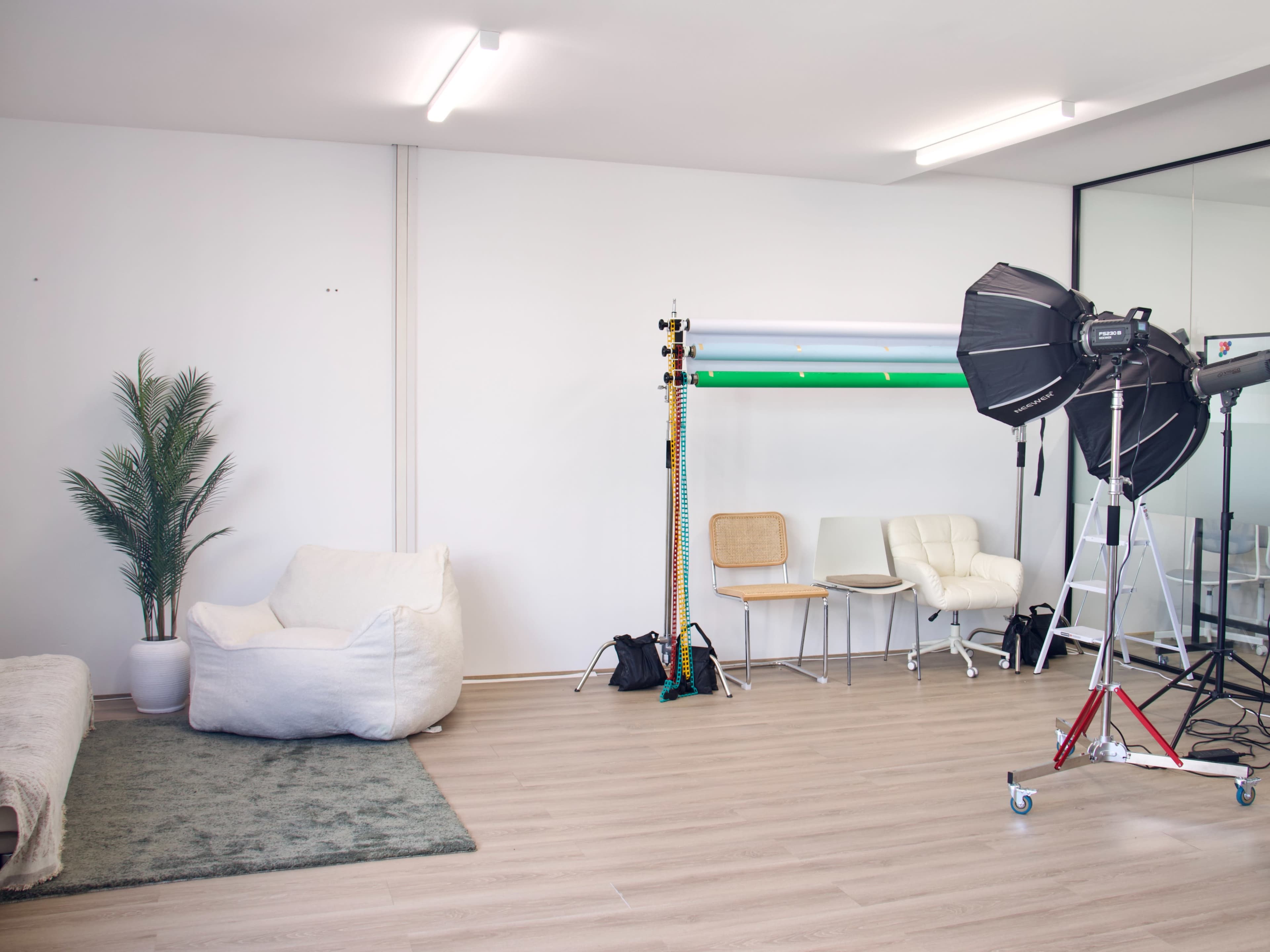 The image shows a bright photo studio with a green background setup, chairs, and a soft seating area.