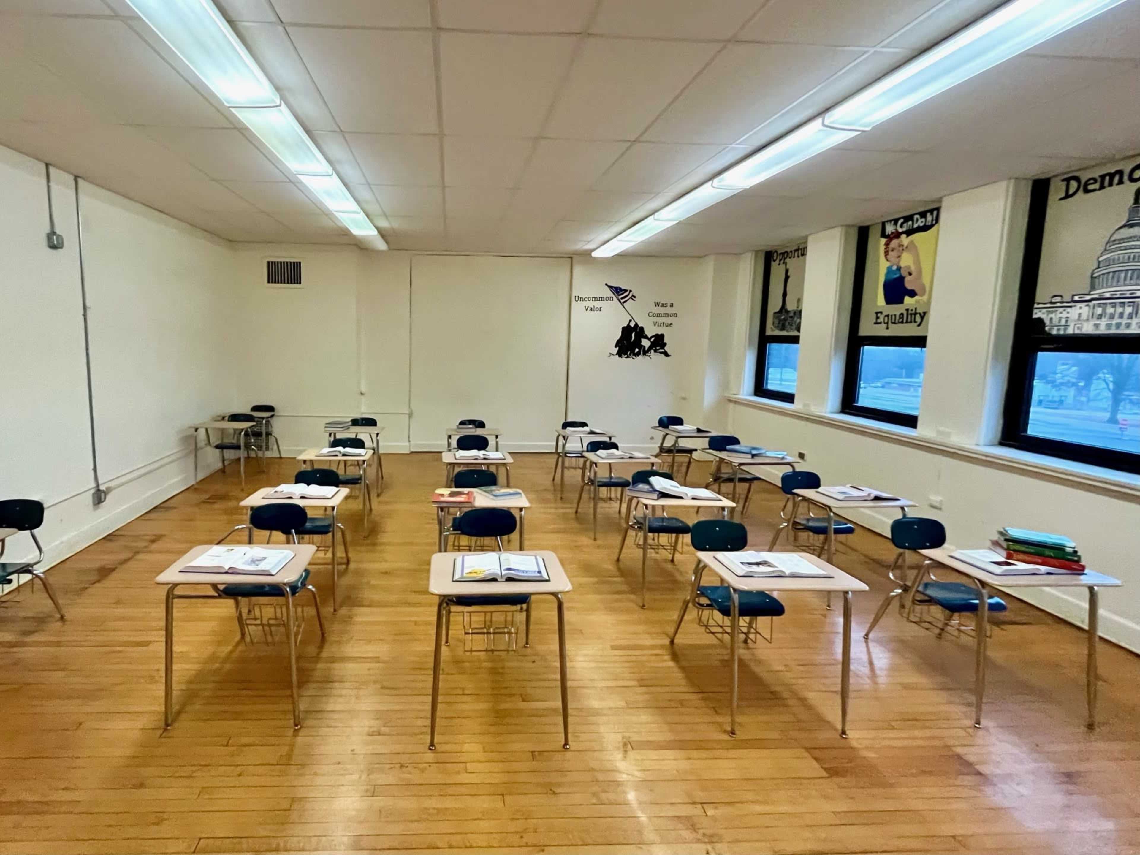 The image shows a classroom with multiple desks arranged in a grid, each with a notebook and several desks empty.