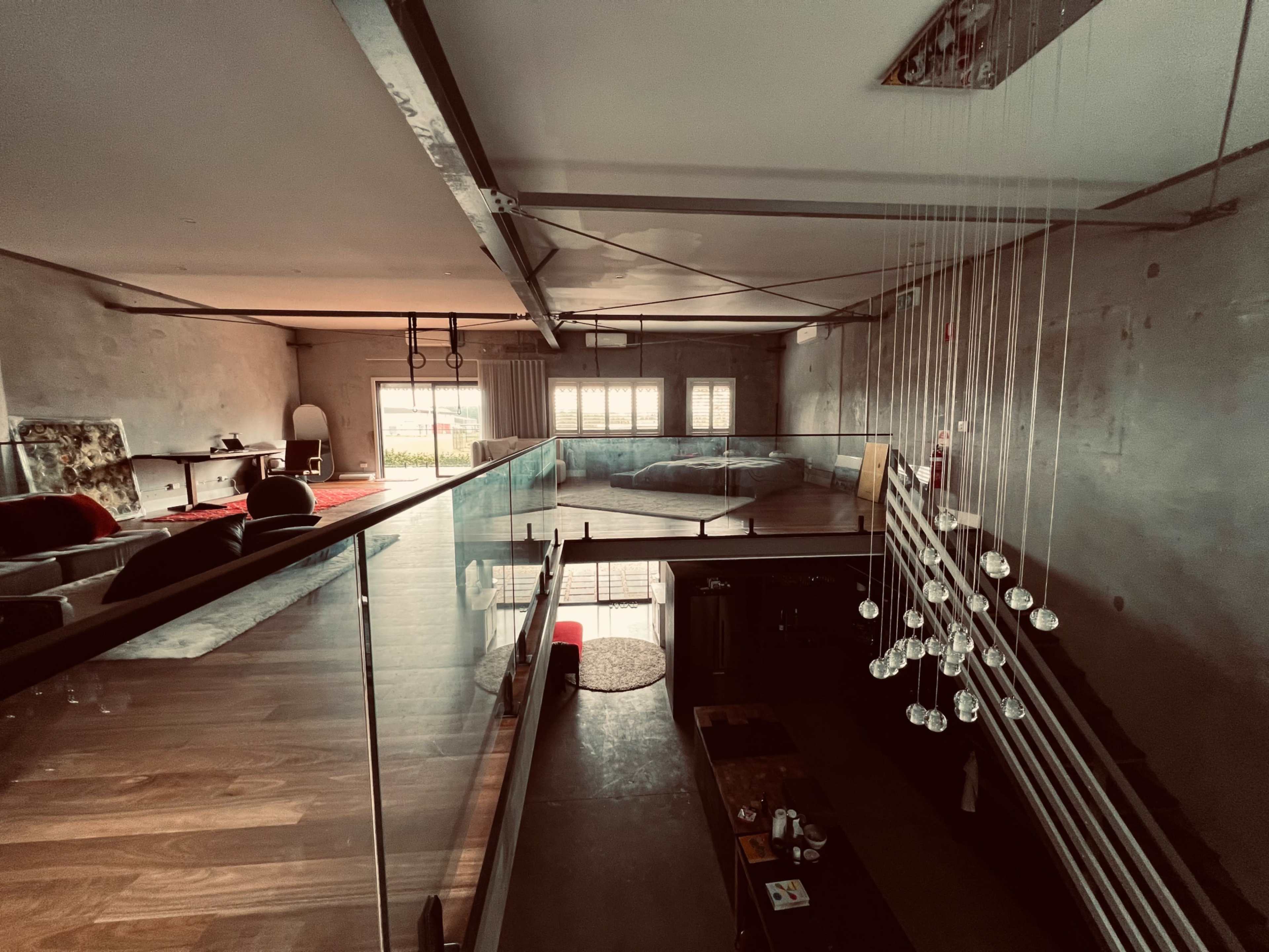A modern, spacious loft with open areas, glass railings, and a view of a seating area and a bed on the upper level.