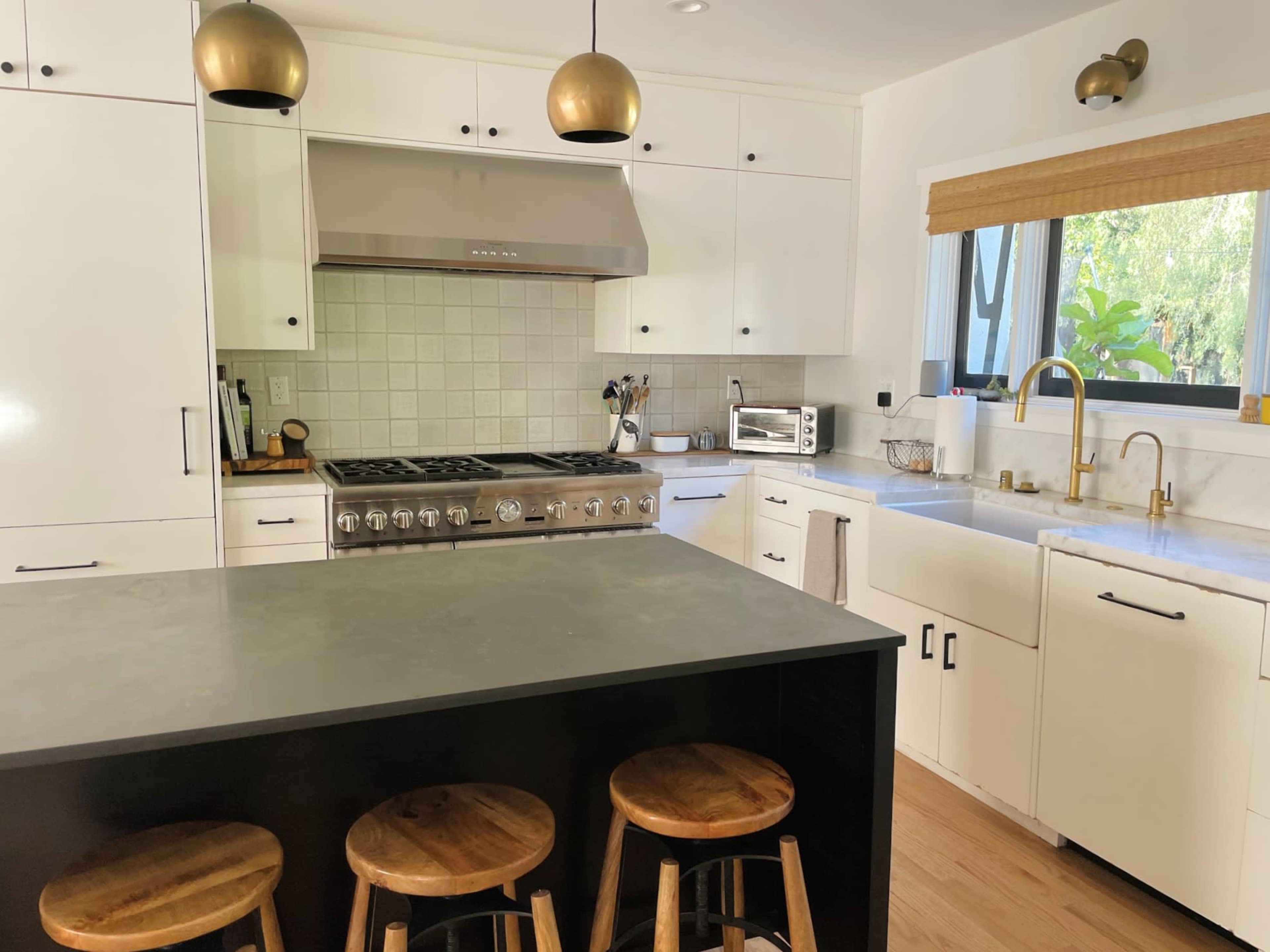 A modern kitchen features a large stainless steel stove, a marble sink, and an island with wooden stools.