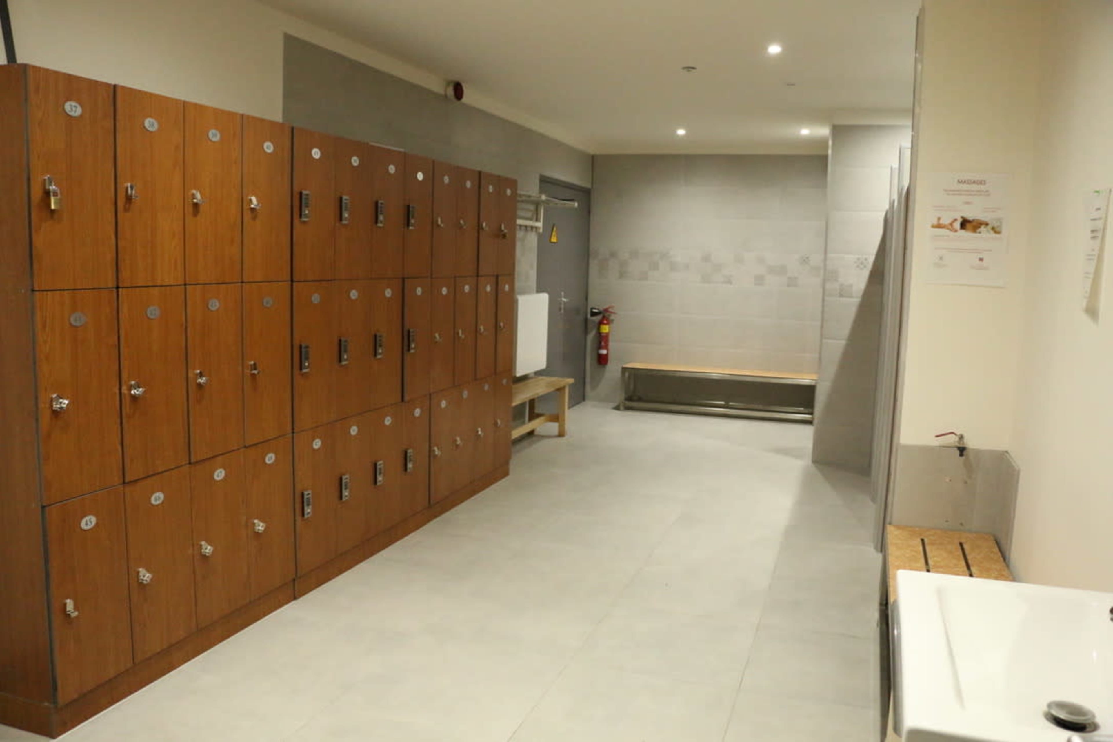 A locker room with wooden lockers along one side, a bench area, and a sink in the corner.