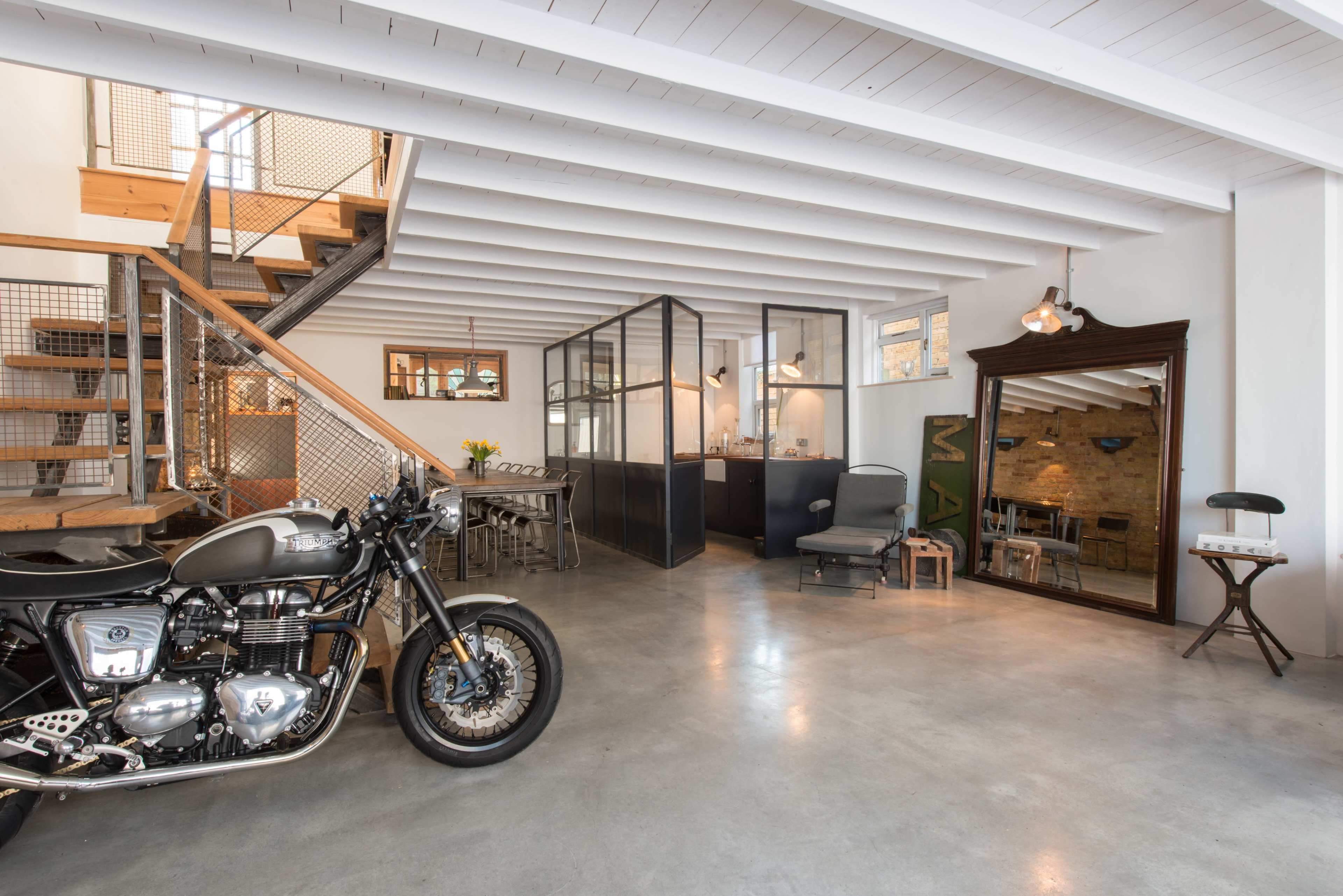The image shows a spacious, modern interior featuring a motorcycle, a dining area, a staircase, and glass-walled rooms.