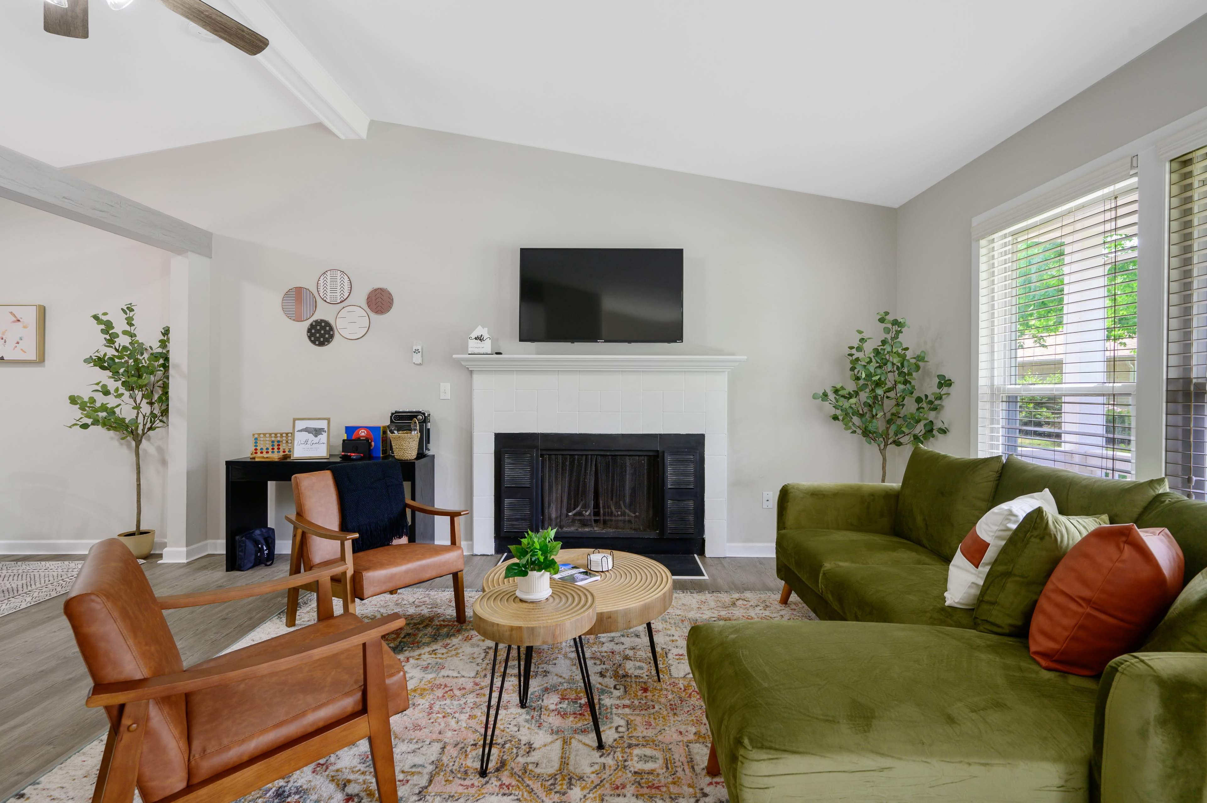 The image shows a living room with a green sofa, wooden chairs, a coffee table, a fireplace, and a mounted television.