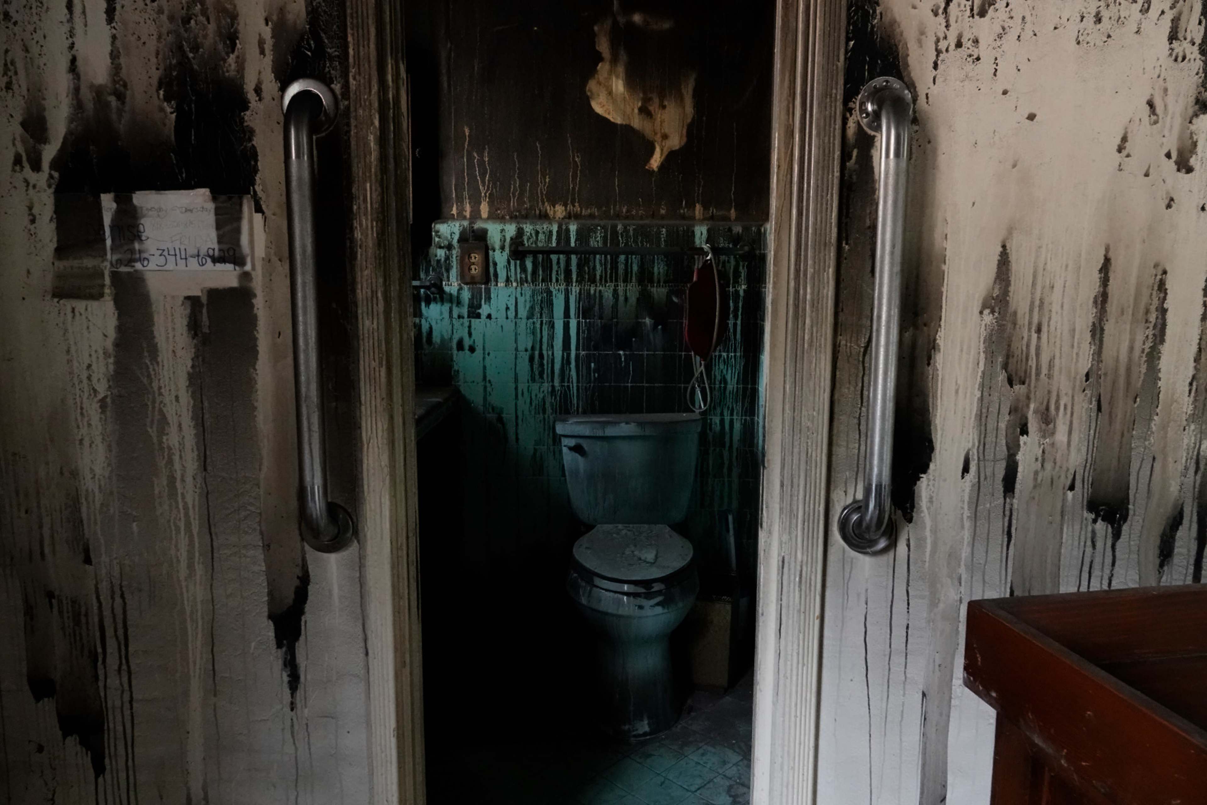 The image shows a bathroom with a partially visible toilet, surrounded by soot-stained walls.