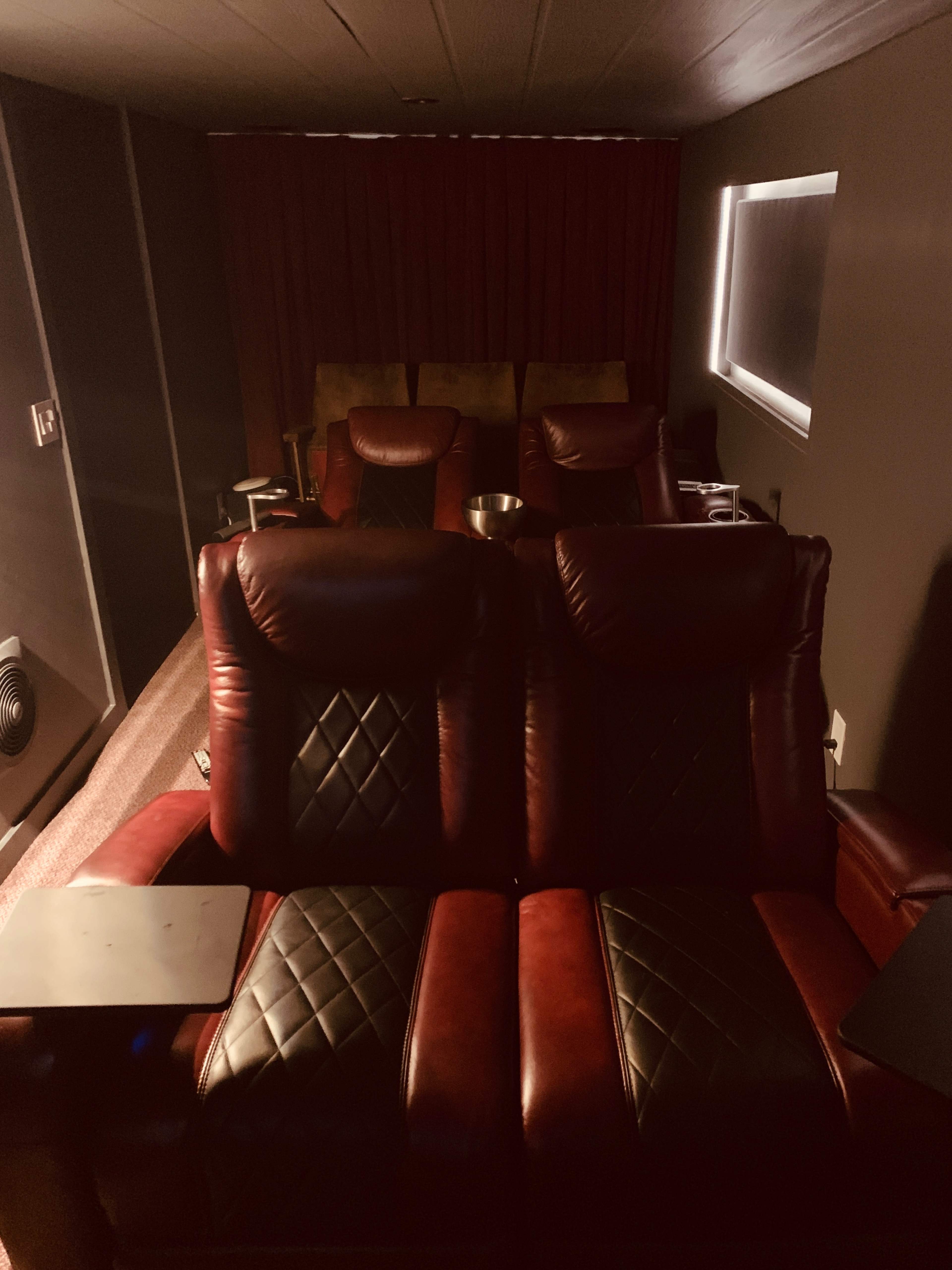 A dimly lit home theater with plush red recliners arranged in a row, accompanied by side tables and a bowl.
