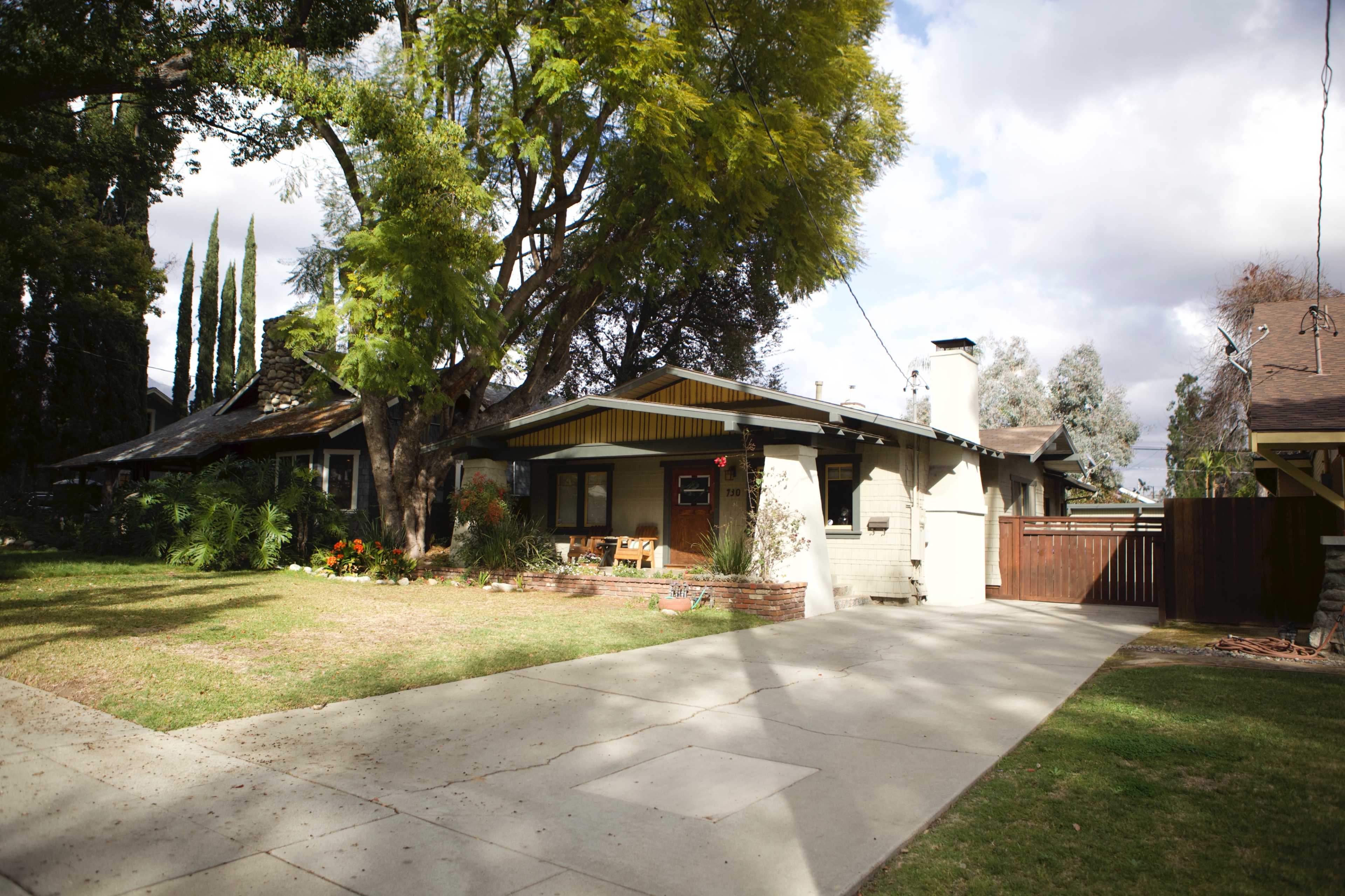 The image shows two houses on a residential street, with a well-maintained lawn and a concrete driveway leading to one of the homes.