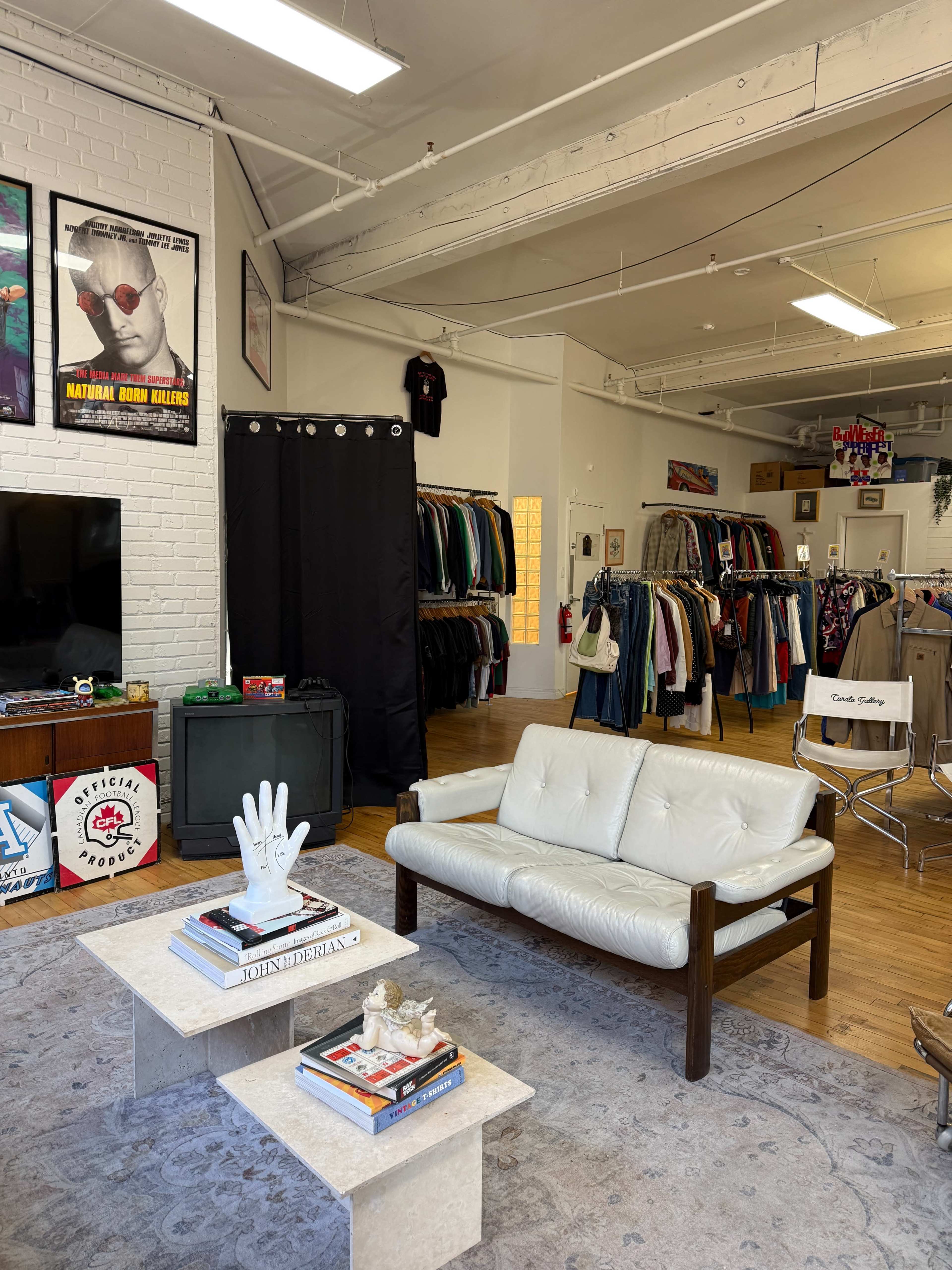 The image shows a vintage-inspired shop interior with a white sofa and a coffee table in the foreground, while clothing racks line the walls in the background.