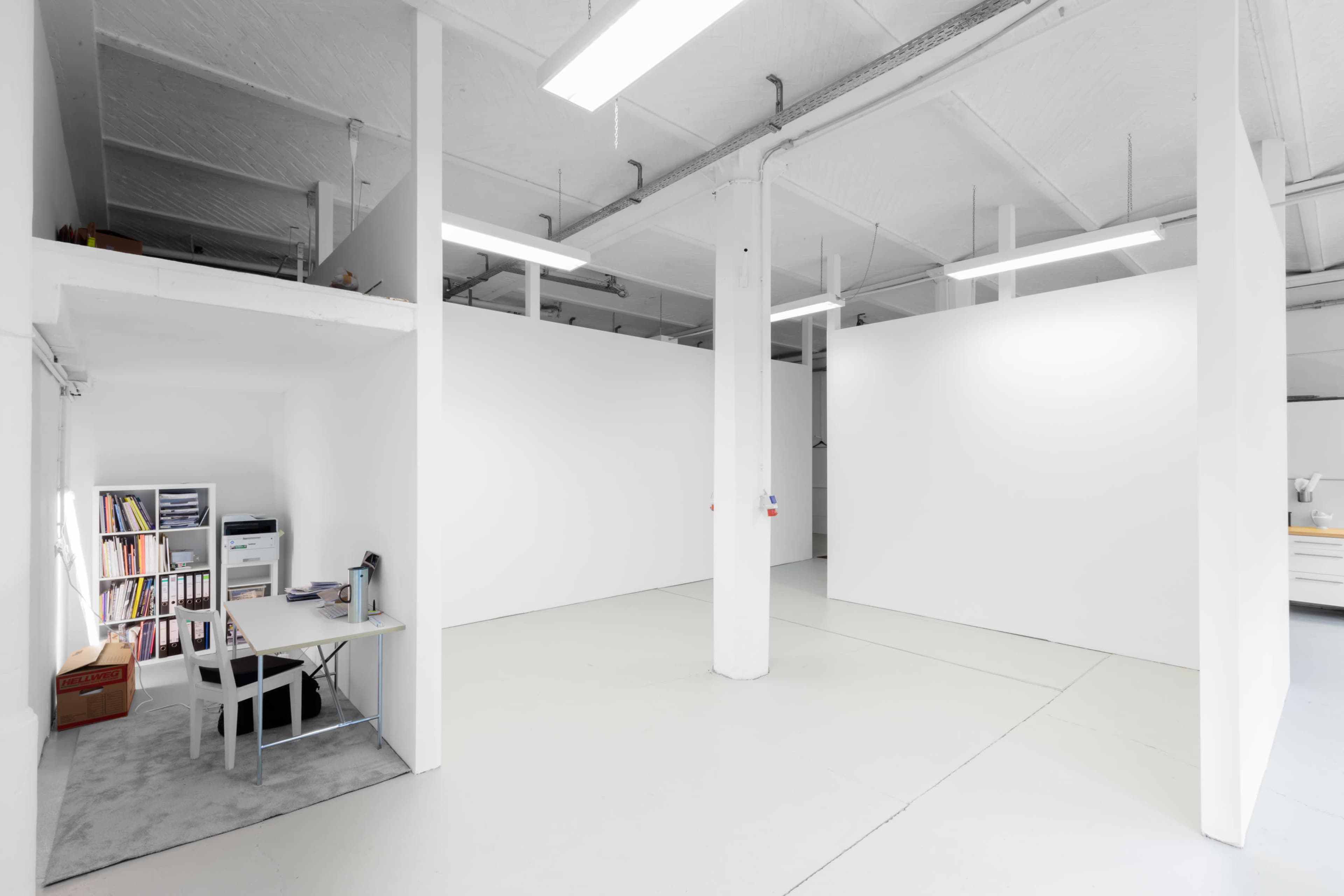 A spacious, minimalist open office with white walls and a desk arrangement in one corner.