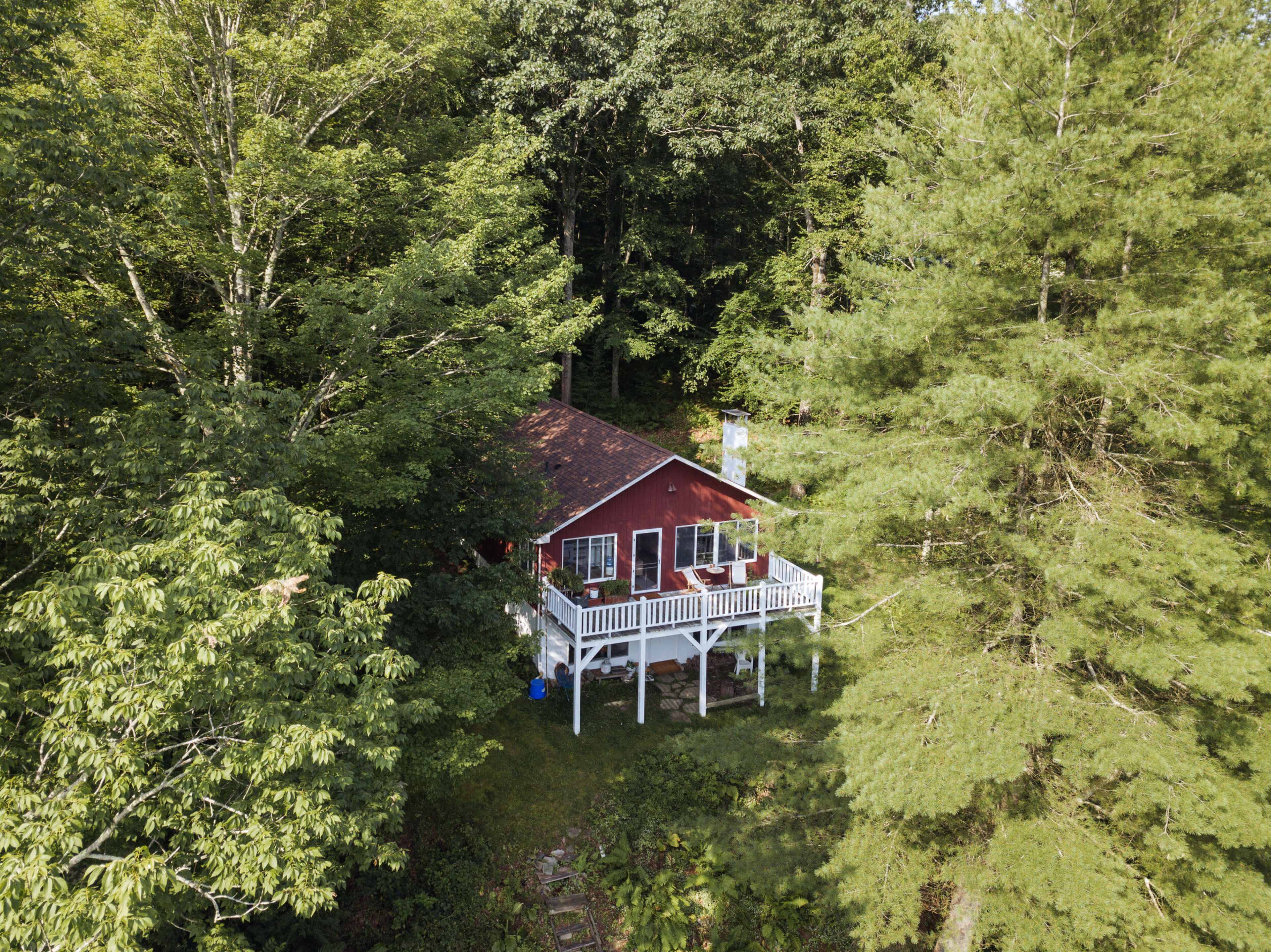 A small red house is situated on a wooden deck surrounded by dense green trees.