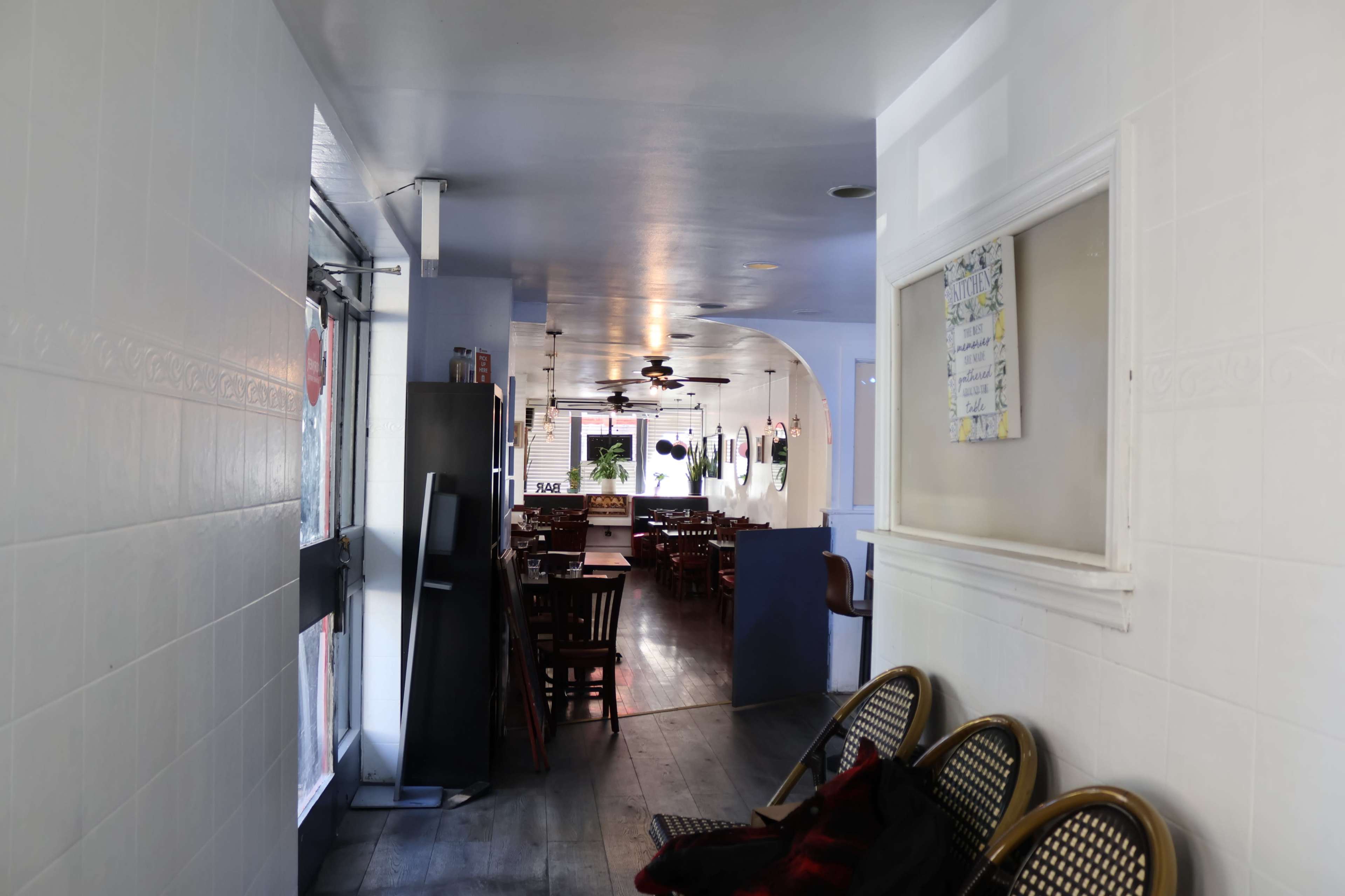 The image shows a corridor leading to a dining area with wooden chairs and tables, illuminated by overhead lights.