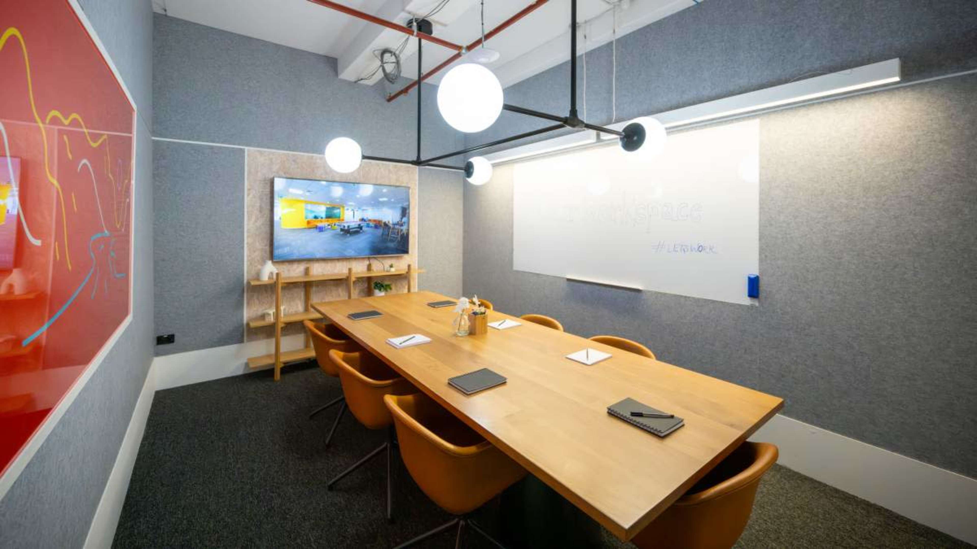 A modern conference room features a large wooden table surrounded by stylish chairs, a wall-mounted television, and a whiteboard.