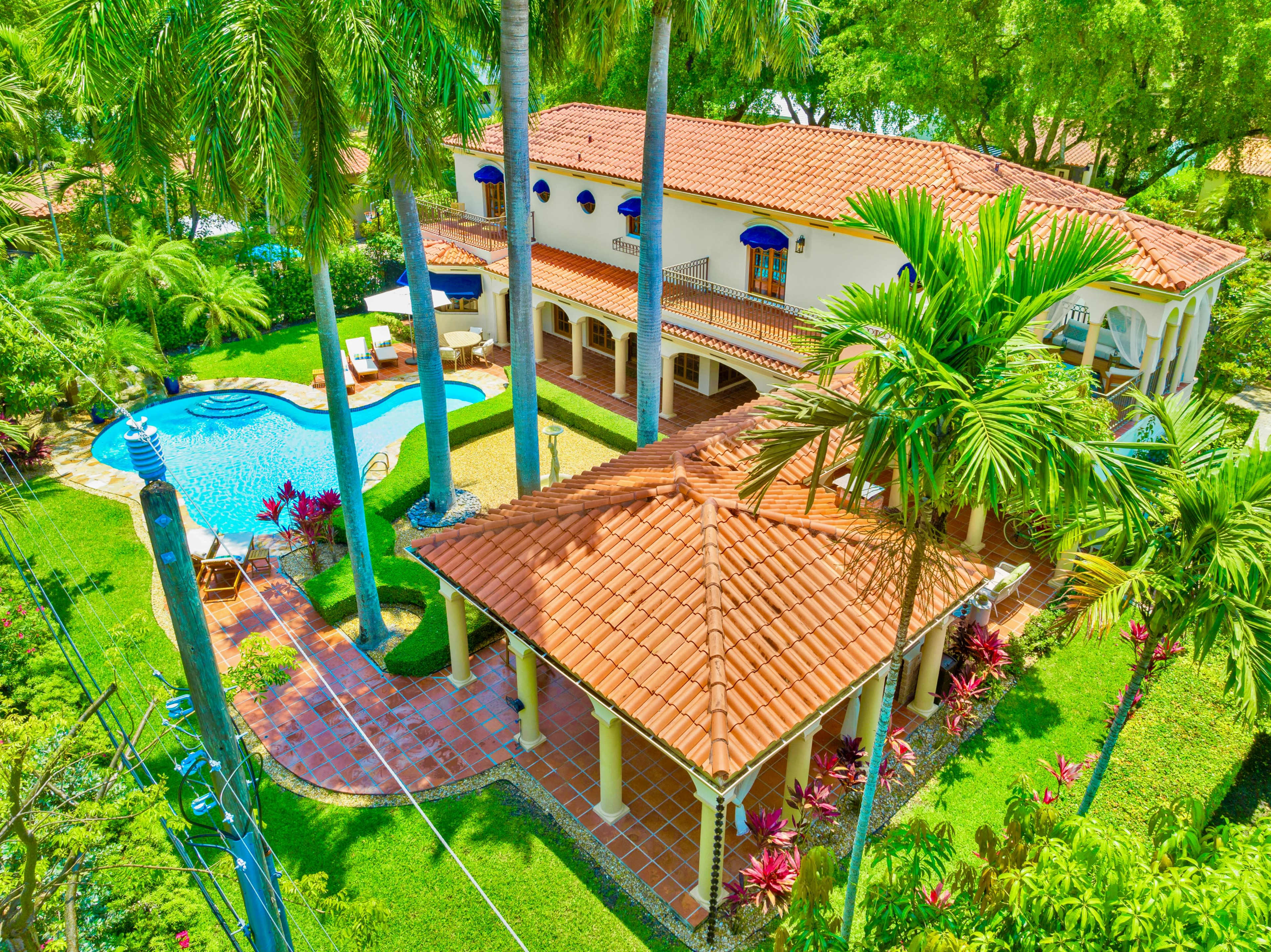 A spacious villa surrounded by palm trees, featuring a swimming pool and a separate gazebo with a tiled roof.