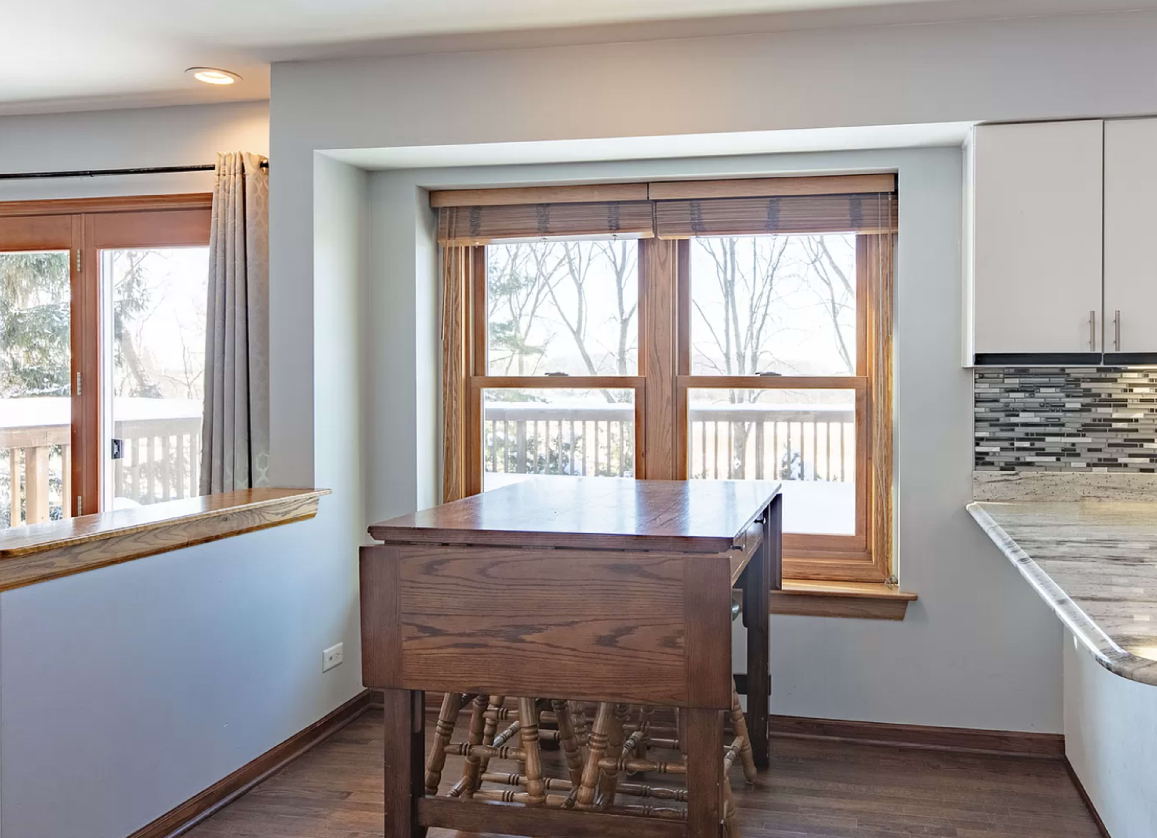 A wooden table with stacked chairs sits in front of a large window overlooking a snowy landscape.