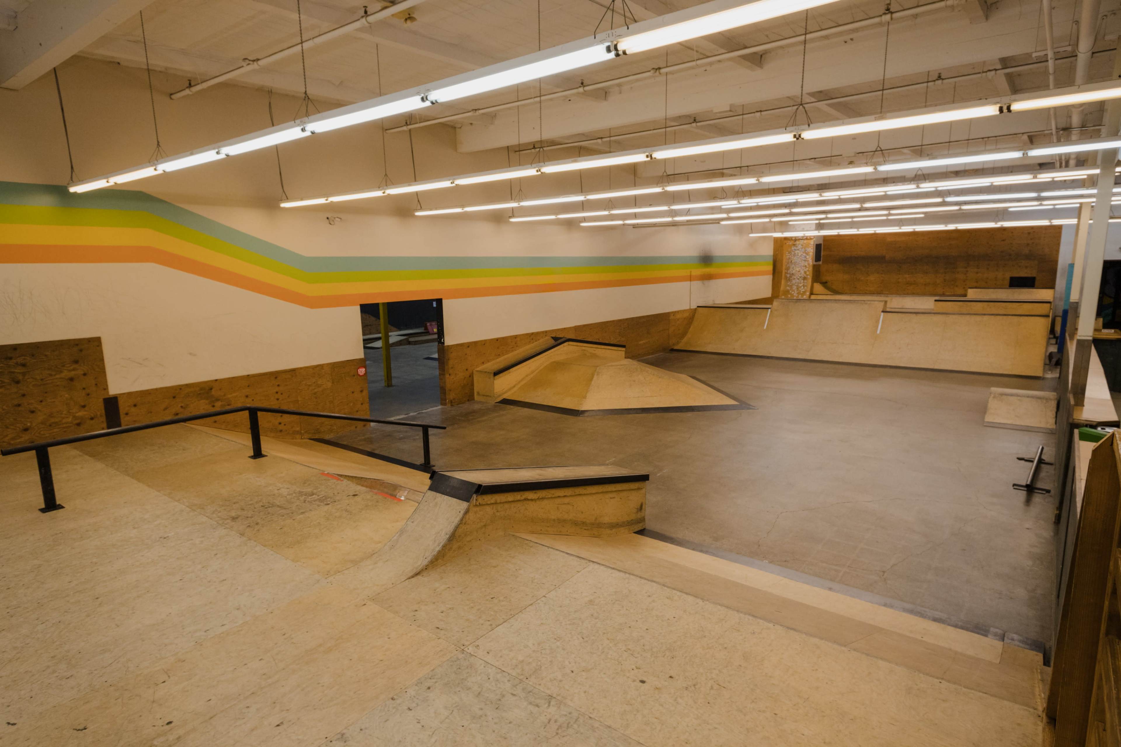 The image shows an indoor skatepark with ramps, ledges, and a colorful striped wall.