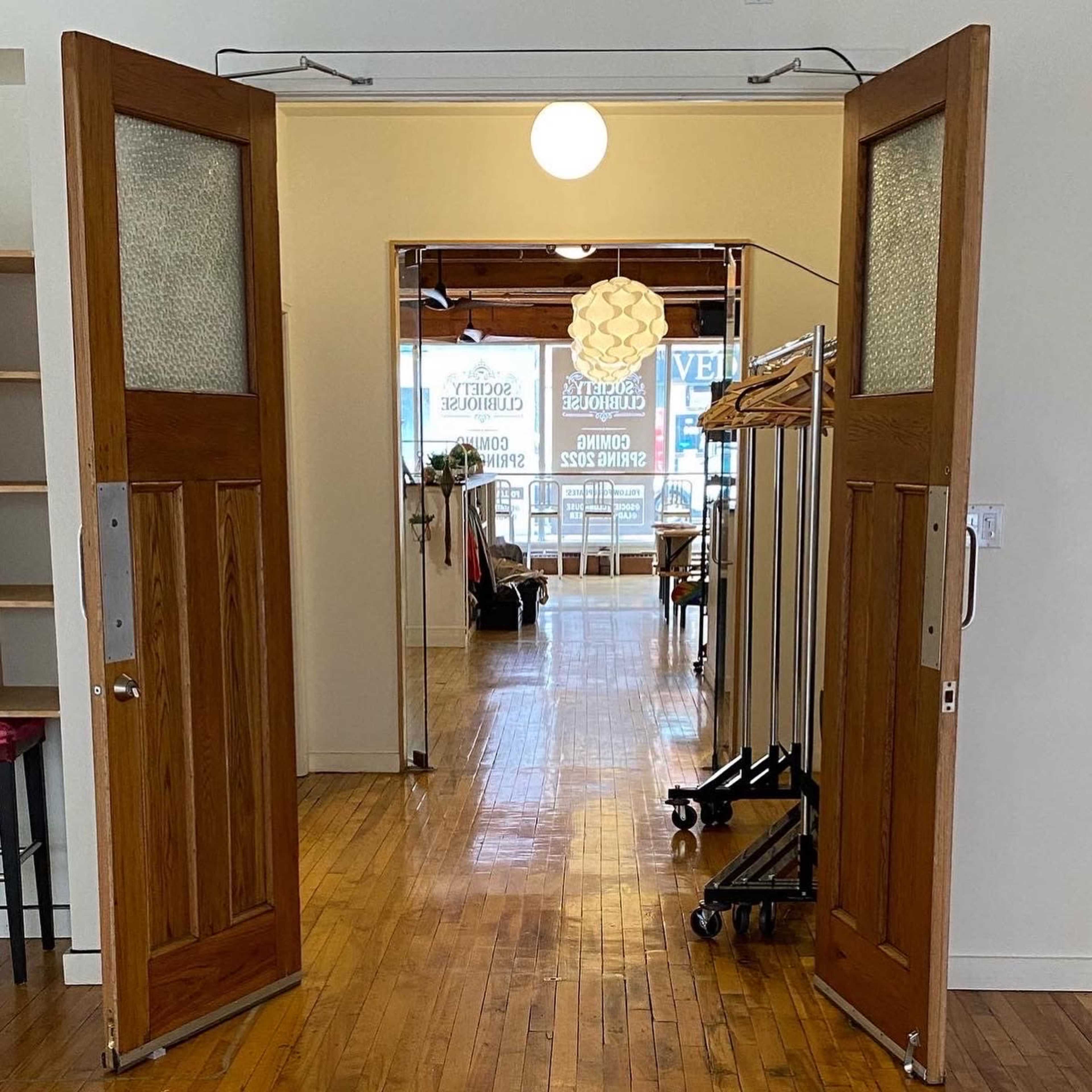 A pair of open wooden doors leading into a well-lit space with clothing racks and a pendant light.