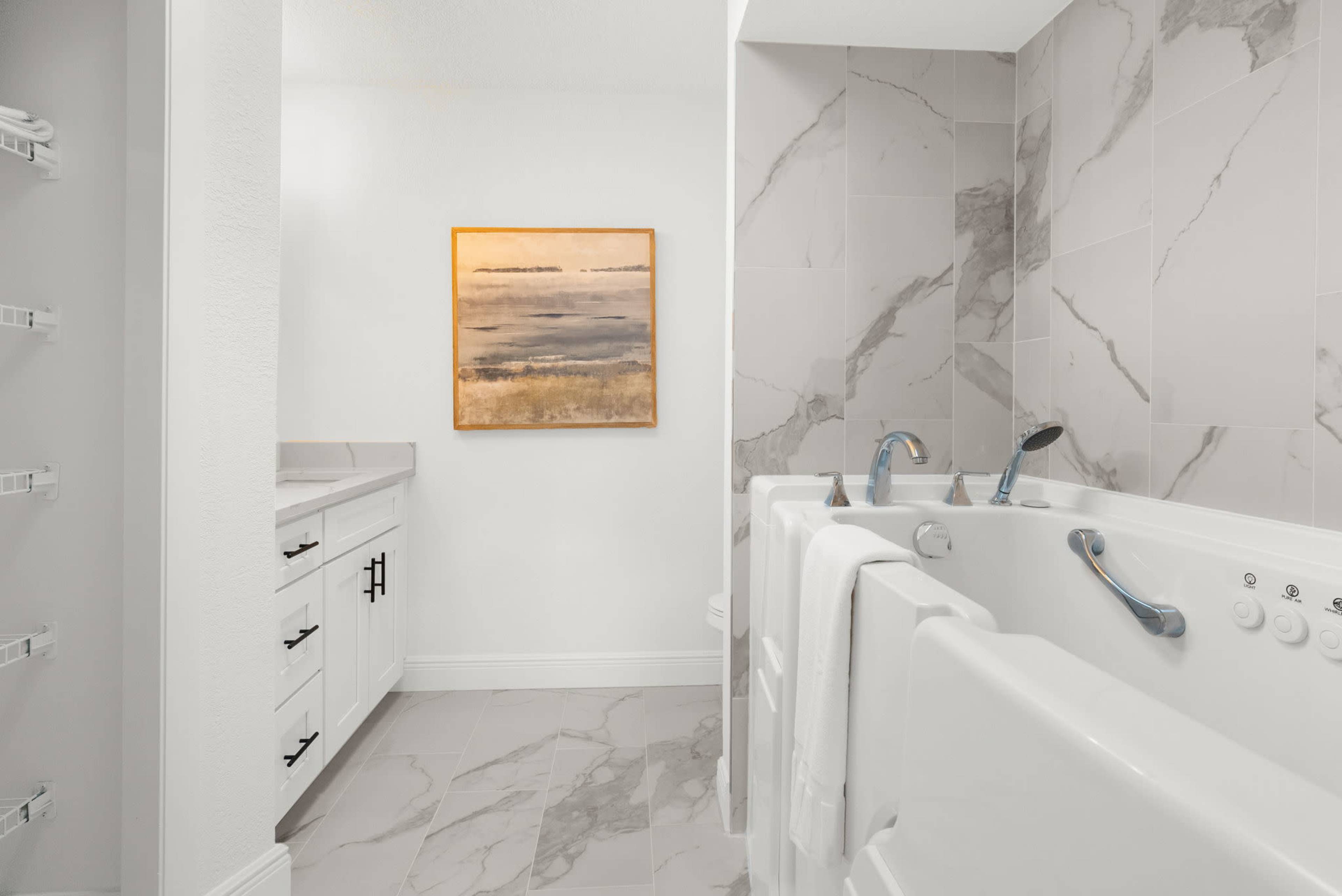 A modern bathroom with a walk-in bathtub, a sink area, and a piece of abstract art on the wall.