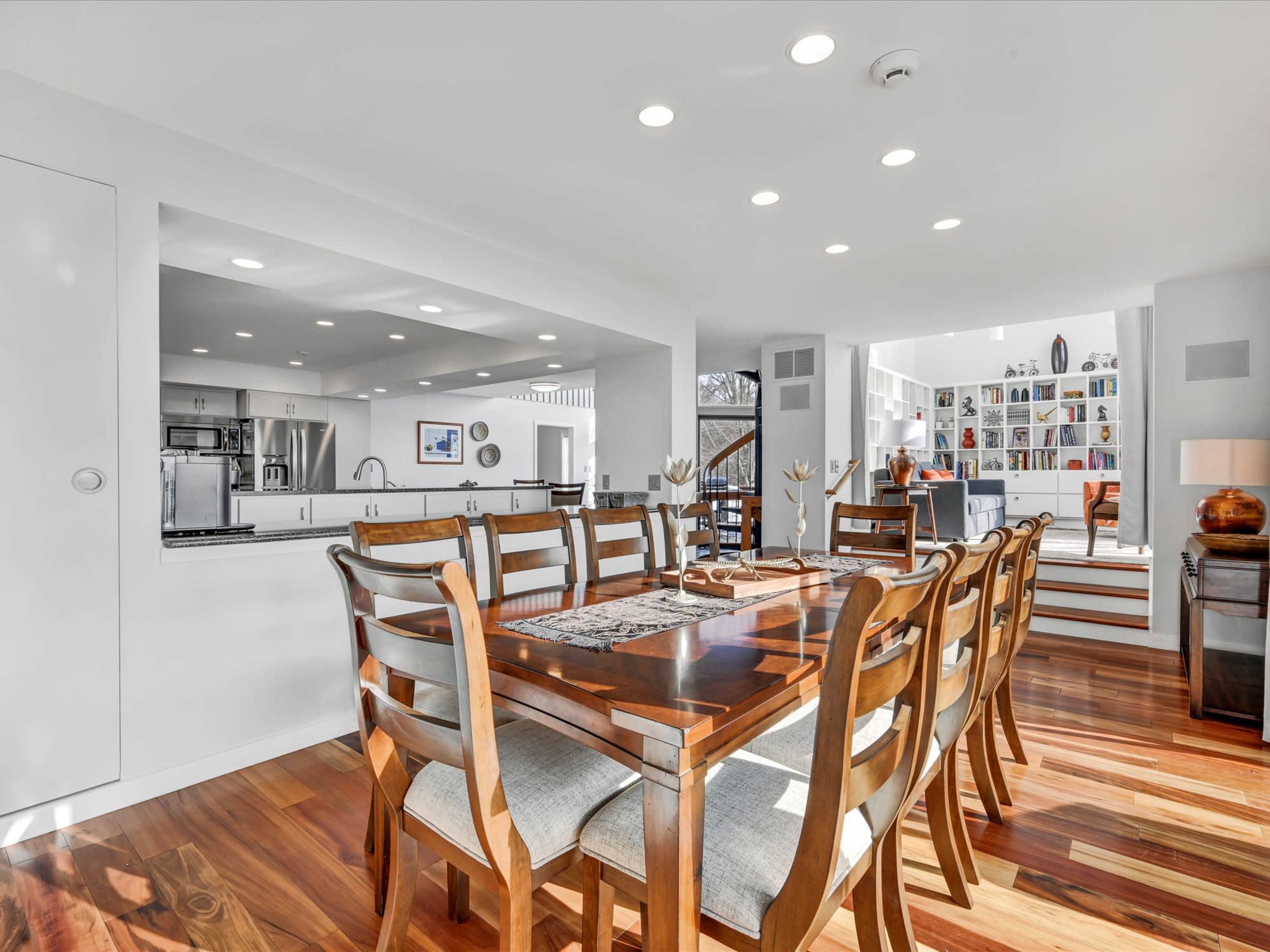 A modern dining area with a wooden table and chairs, leading to an open kitchen and living space filled with bookshelves.