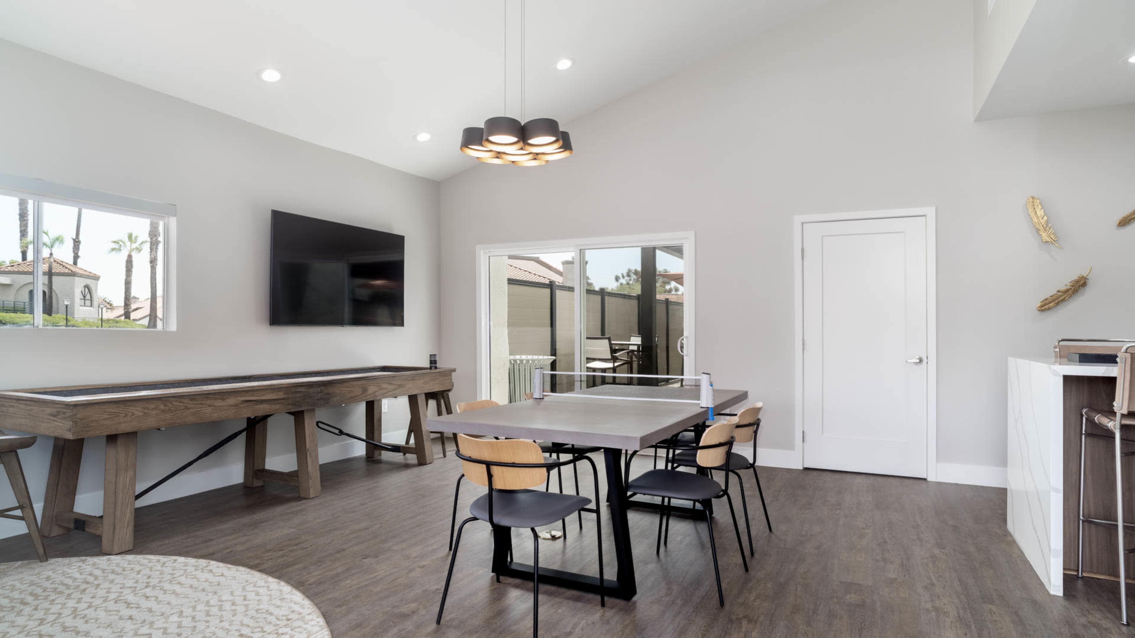 A modern dining area with a wooden table and black chairs, featuring a large flat-screen TV mounted on a light gray wall.