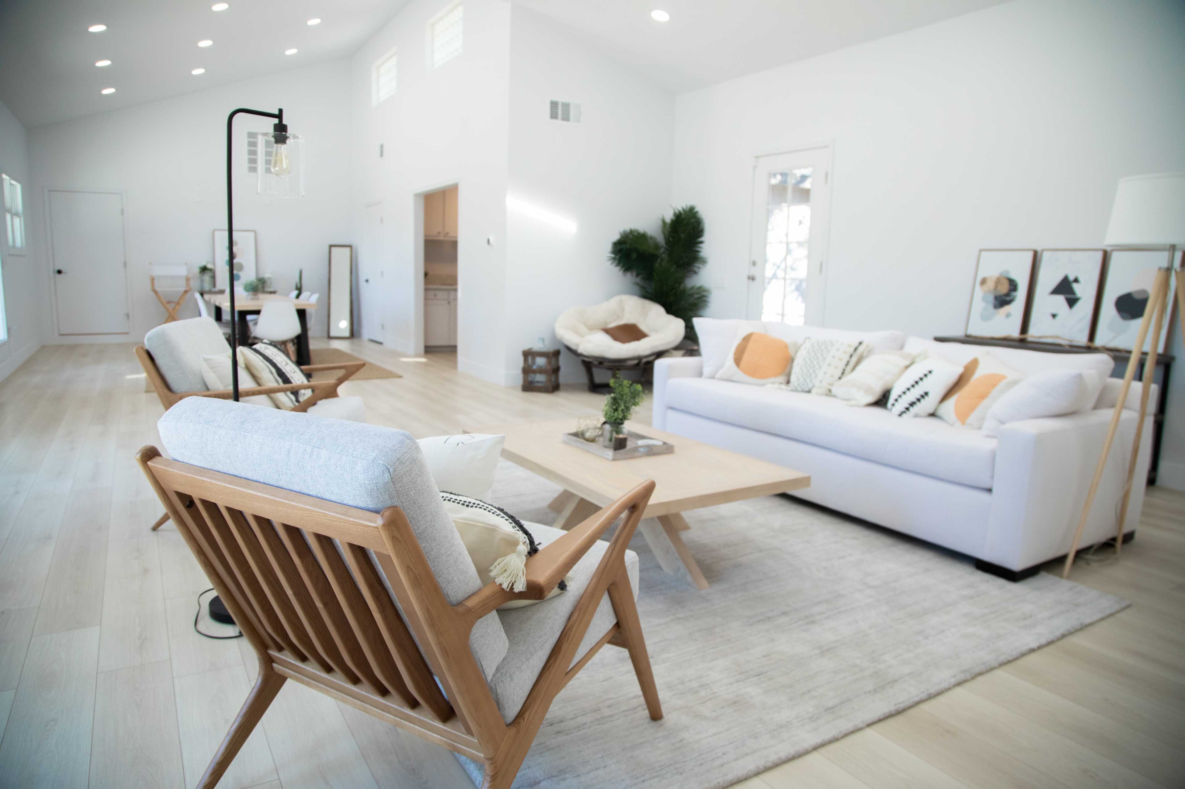 A modern living room with a white sofa, wooden armchairs, a light wooden coffee table, and a neutral area rug, all set against a bright, minimalistic interior.