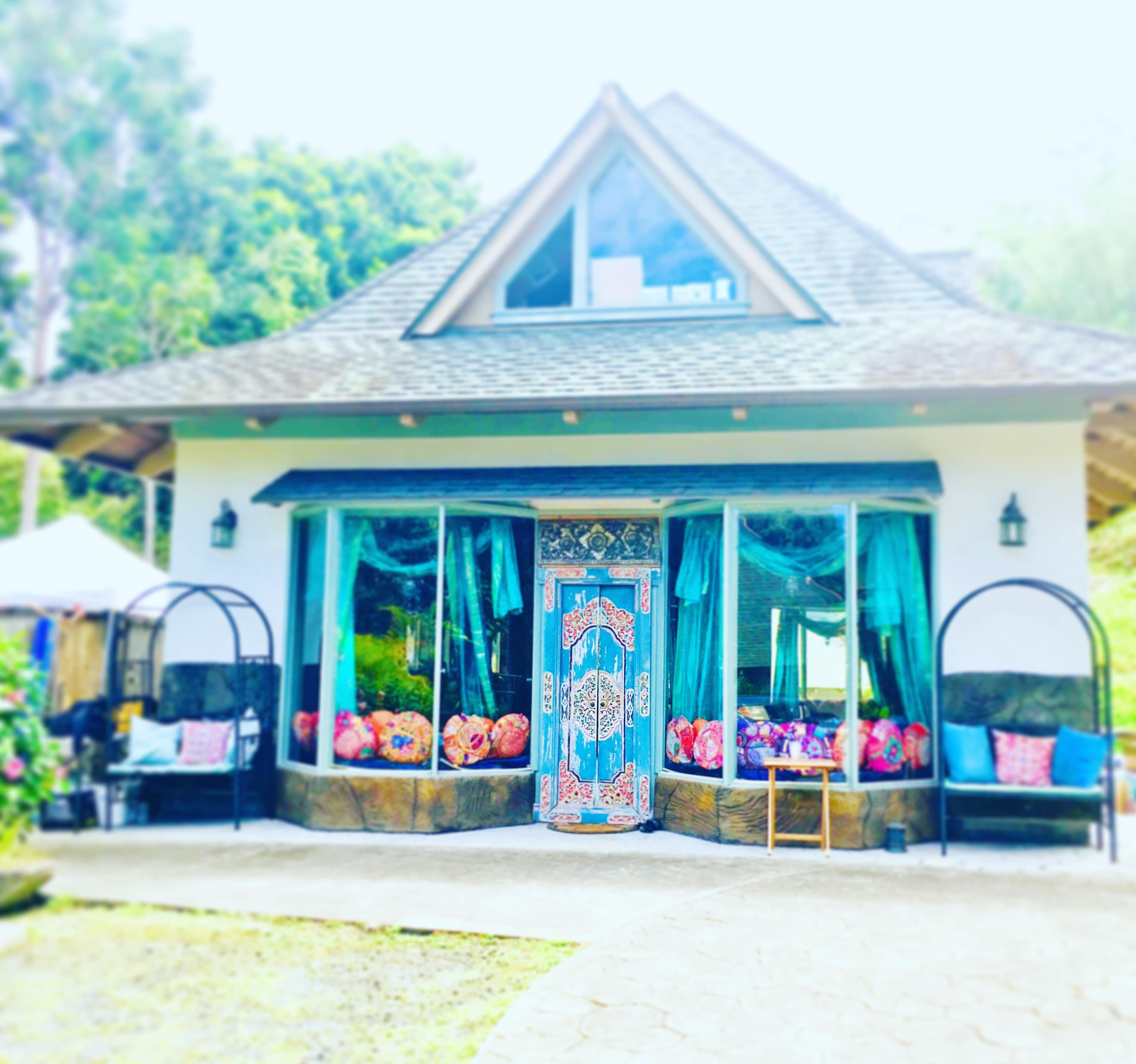 A charming house with a triangular roof and large windows, featuring decorated doors and colorful cushions on outdoor seating.