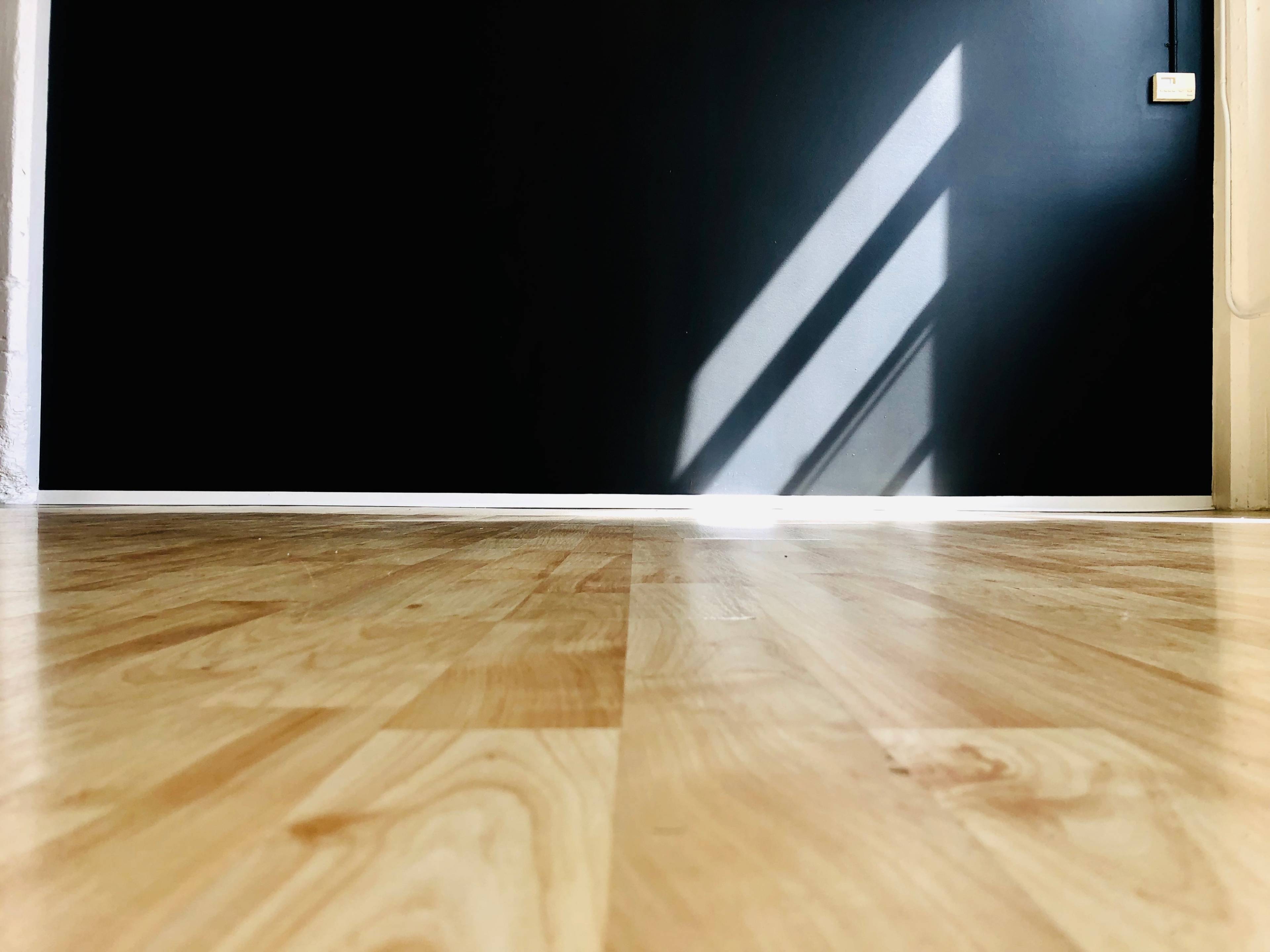 A wooden floor leading to a dark wall with diagonal shadows cast by light.