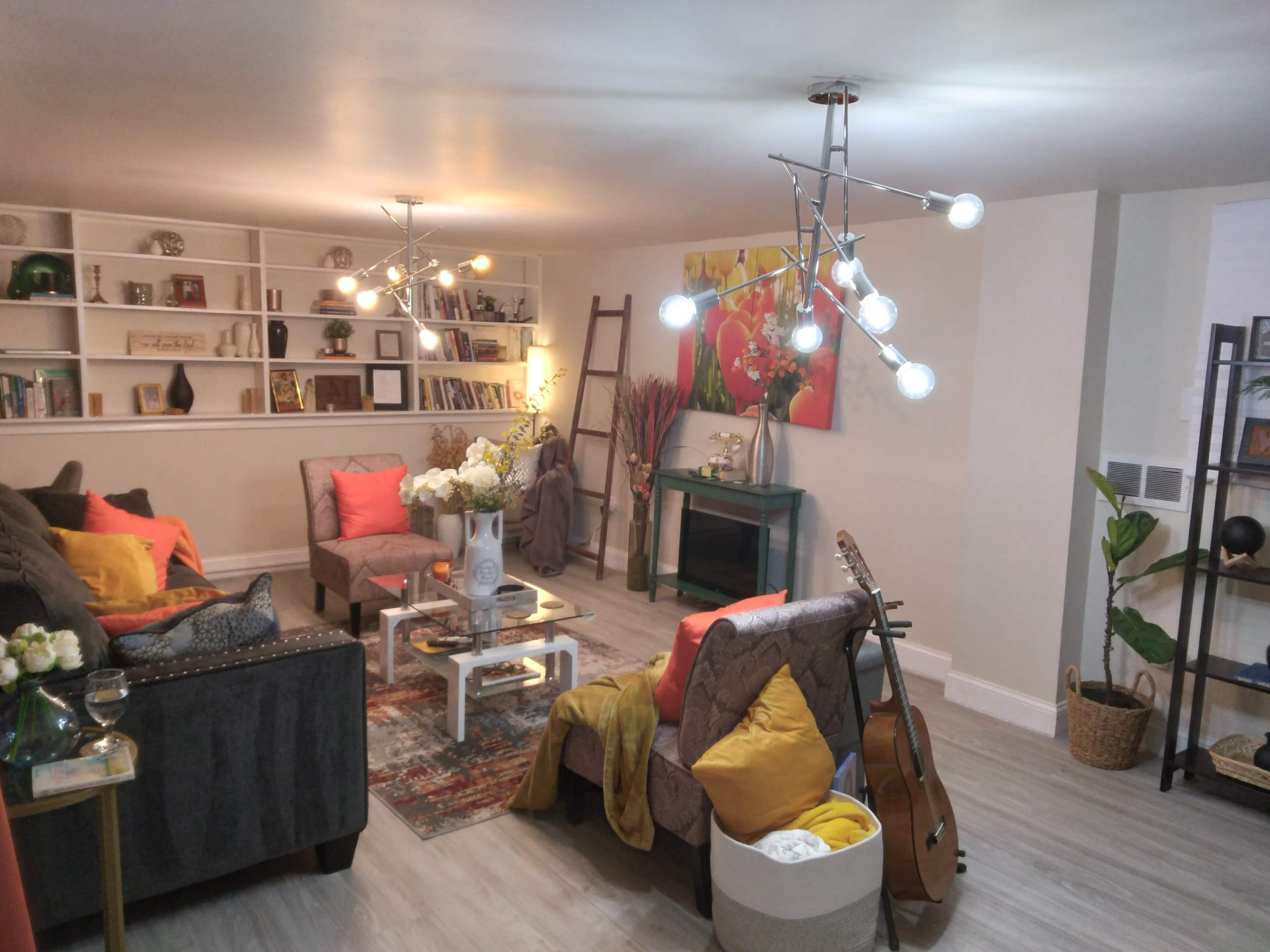 A modern living room with a mix of seating, decorative plants, and a guitar, featuring a light fixture with multiple bulbs.