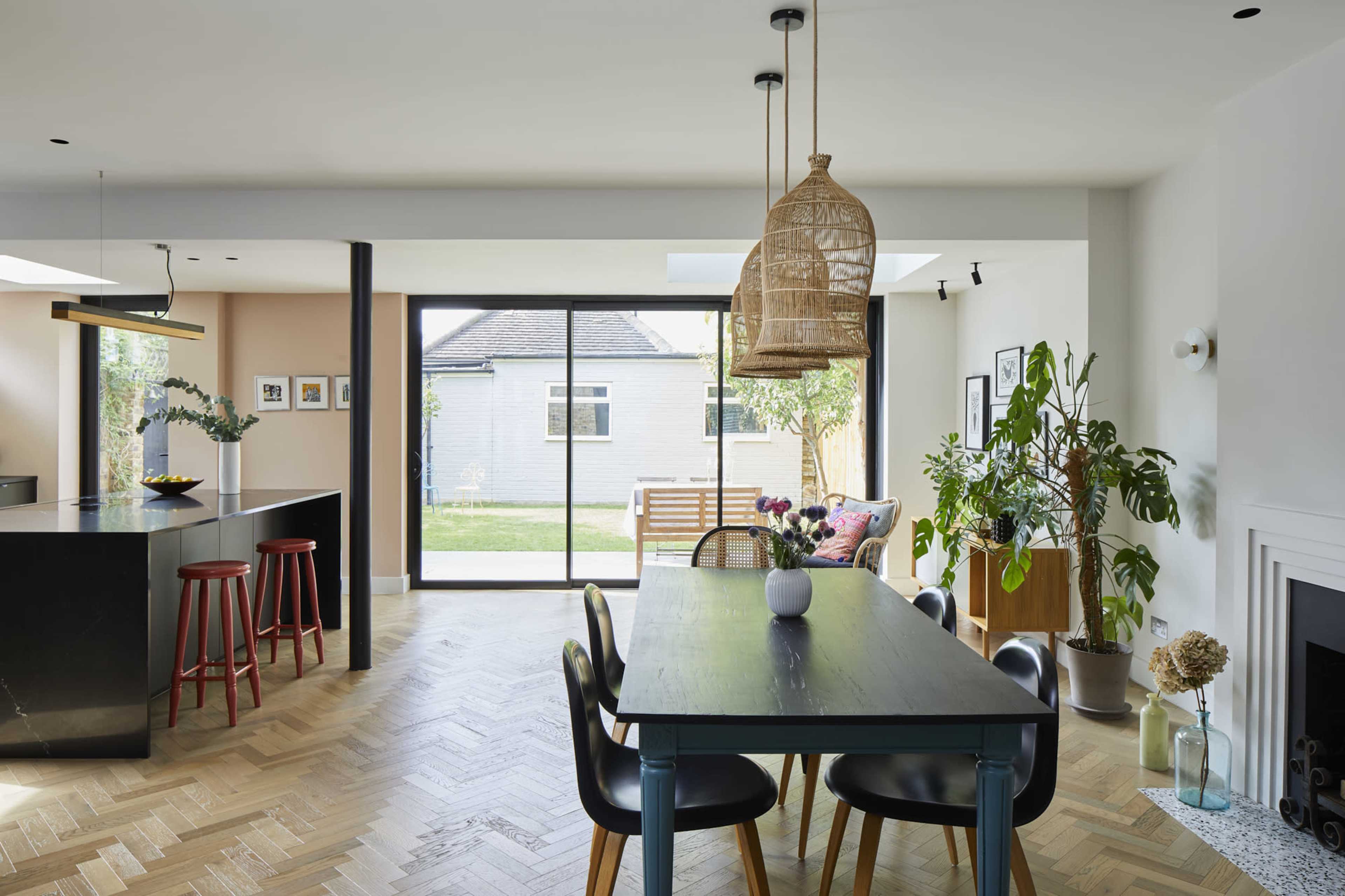A modern kitchen and dining area feature a large table, stylish chairs, and a sliding glass door that opens to a backyard.