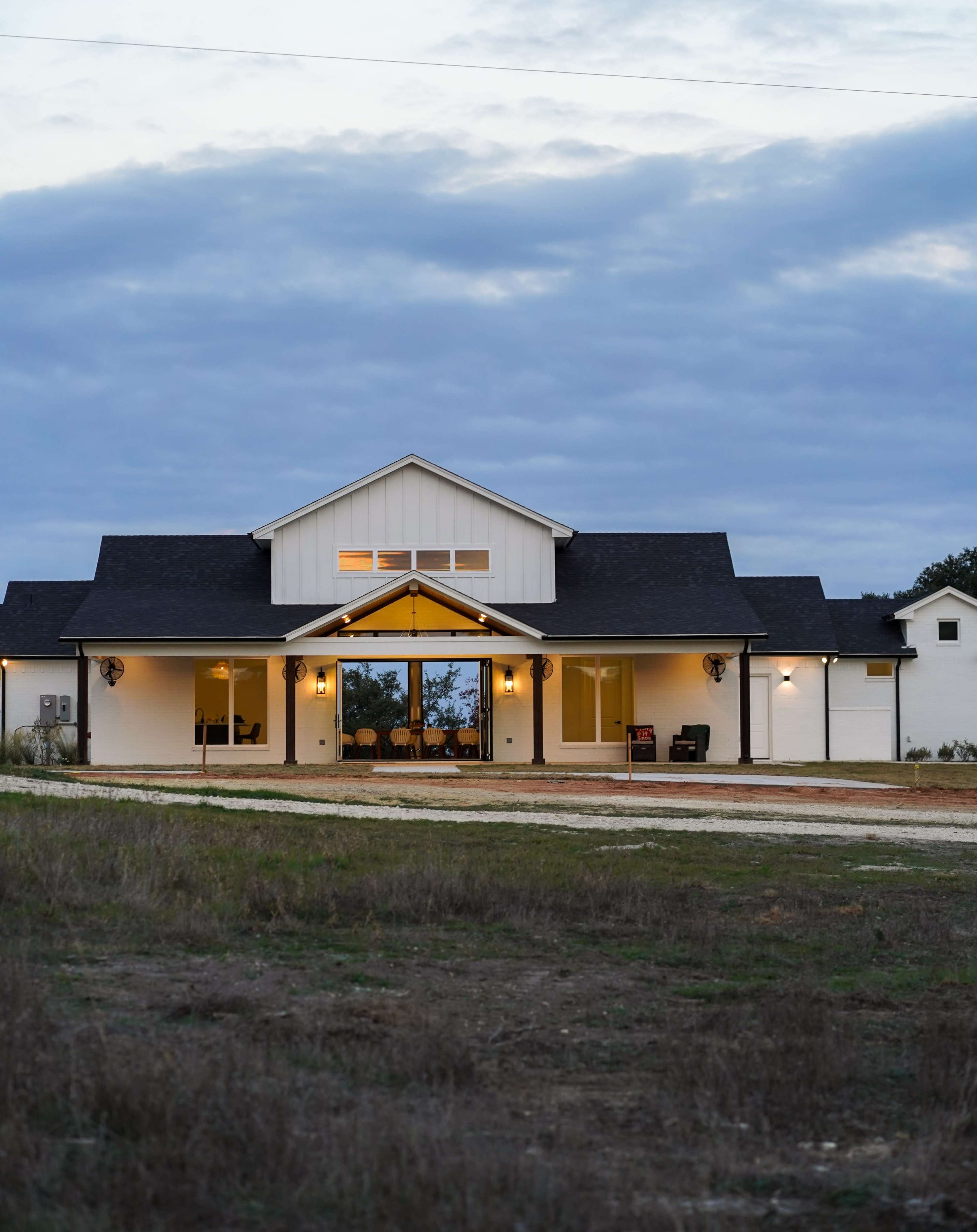 A modern house with a white exterior and a large front porch is set against a cloudy sky.
