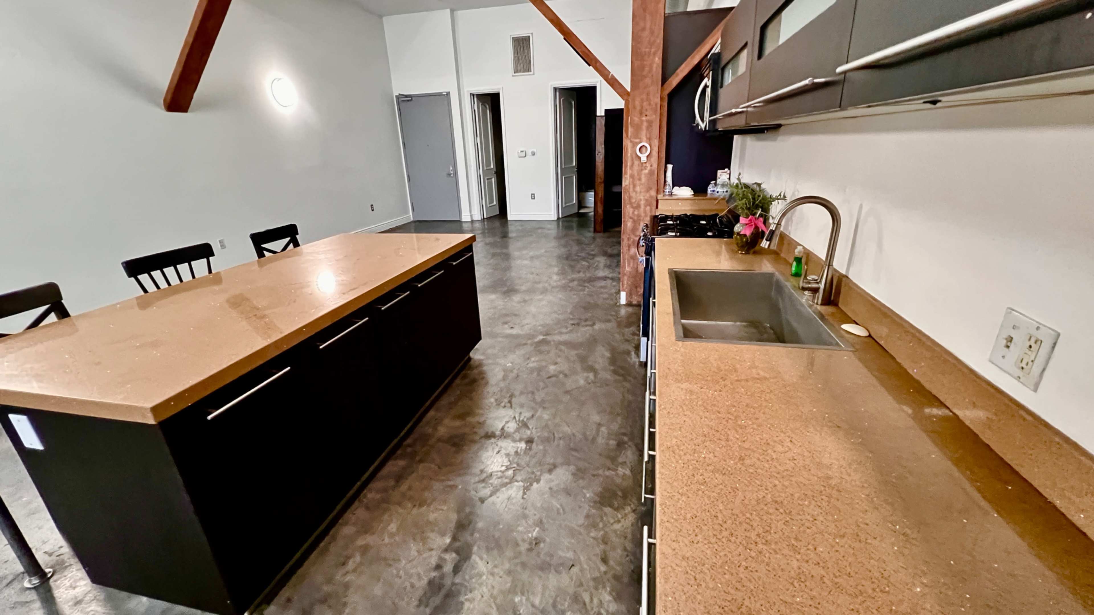 The image shows a modern kitchen with an island, a sink along one wall, and a dining area featuring black chairs.