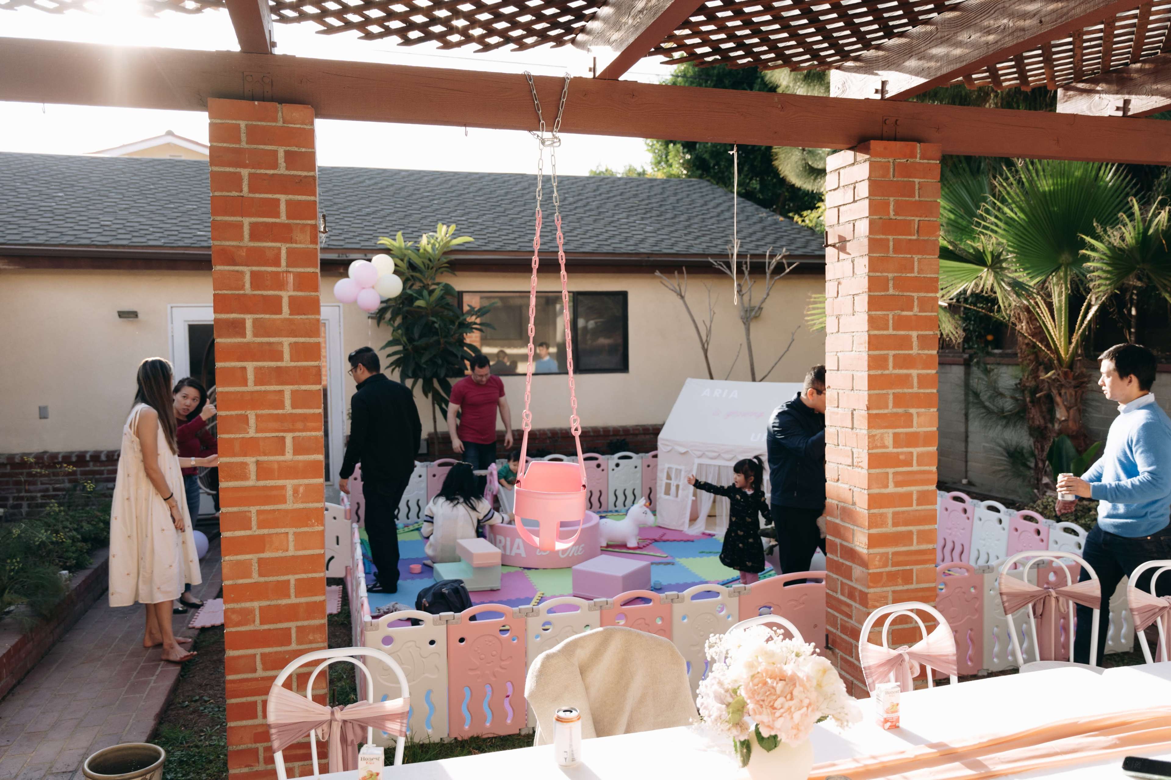 A backyard party is set up with colorful seating and decorations, while guests socialize and children play in a designated area.