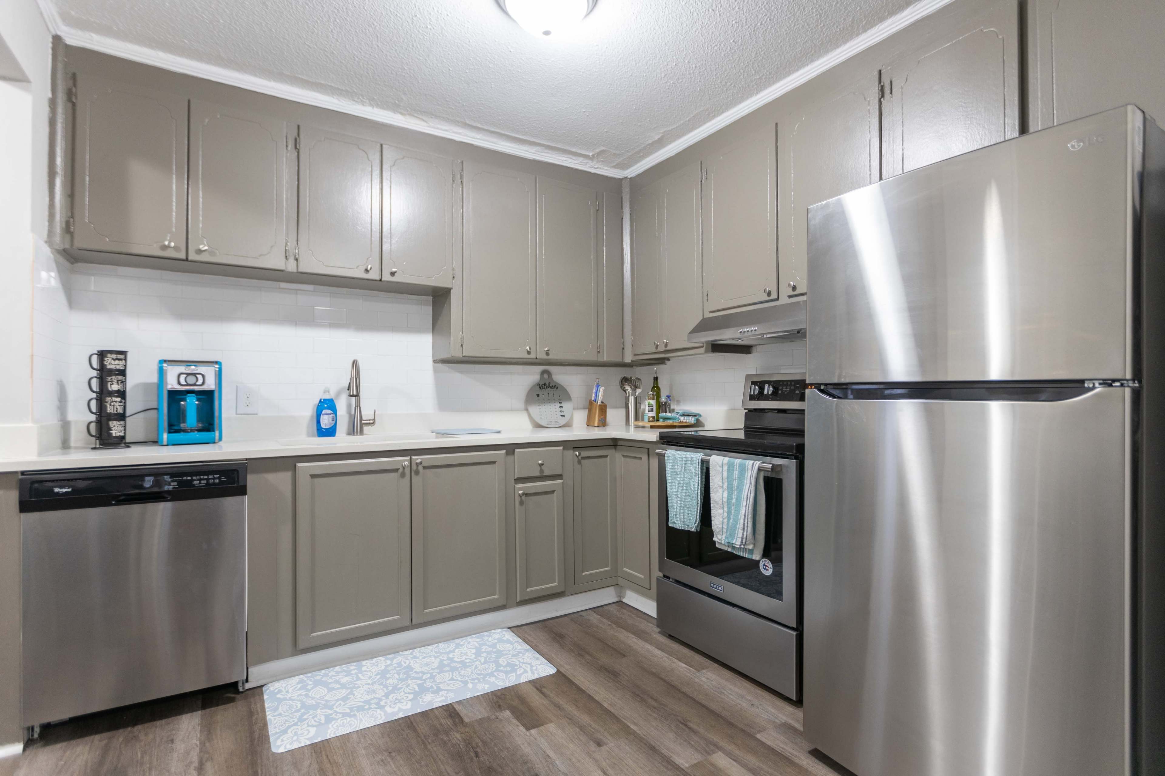 A modern kitchen featuring gray cabinetry, stainless steel appliances, and a light-colored floor mat.