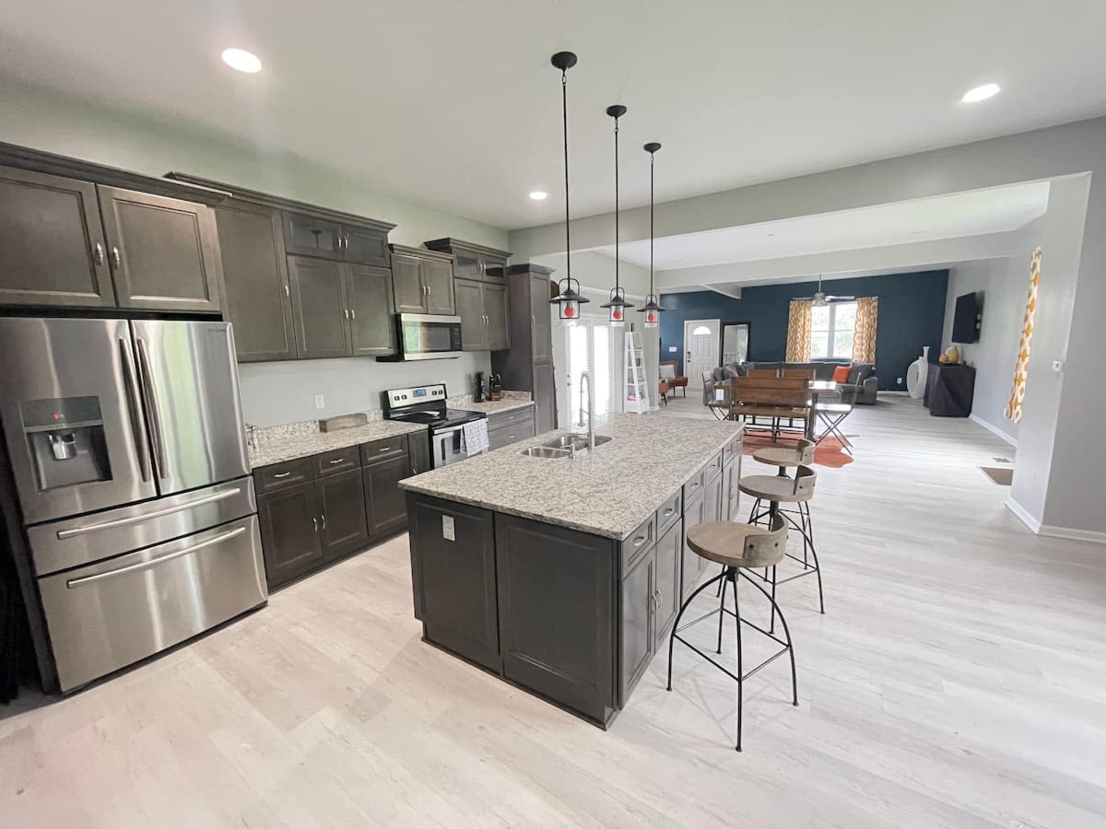 A modern kitchen with dark wooden cabinets, a large island with bar stools, and stainless steel appliances, all illuminated by overhead pendant lights.