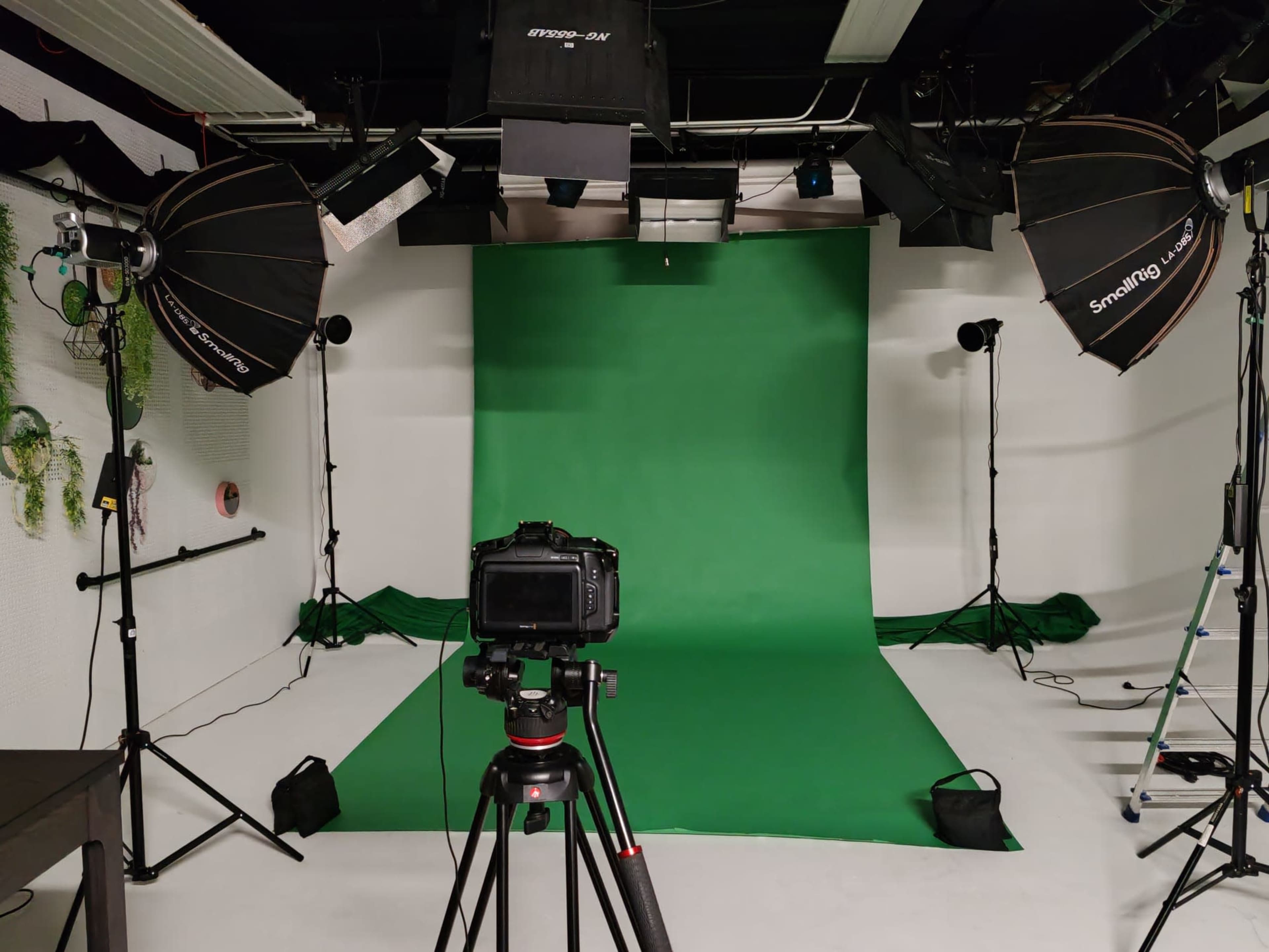 A photography studio is set up with a green backdrop, studio lights, and a camera on a tripod facing the backdrop.