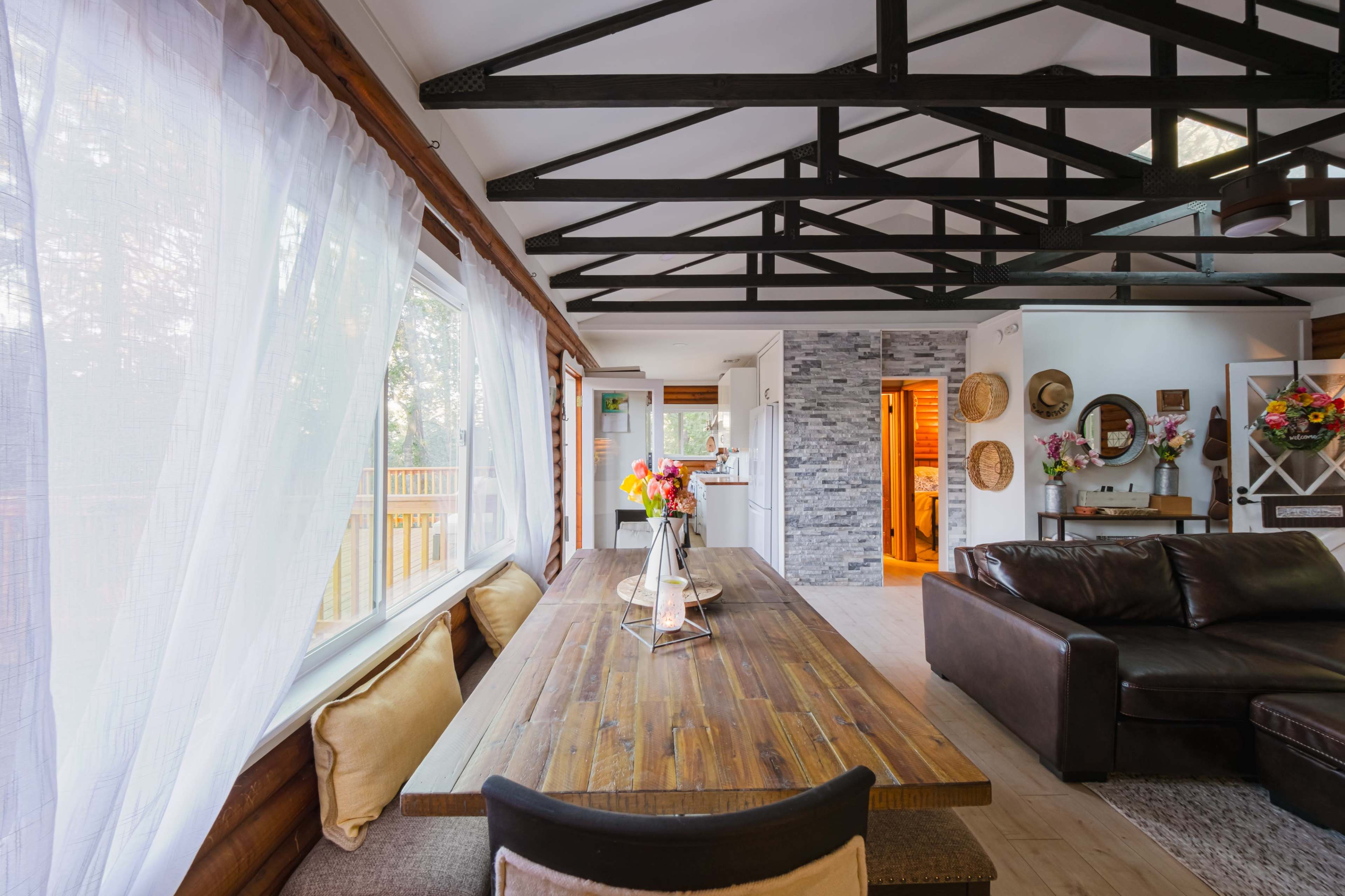 A spacious dining area features a long wooden table with decorative floral arrangements and large windows that allow natural light to fill the room.