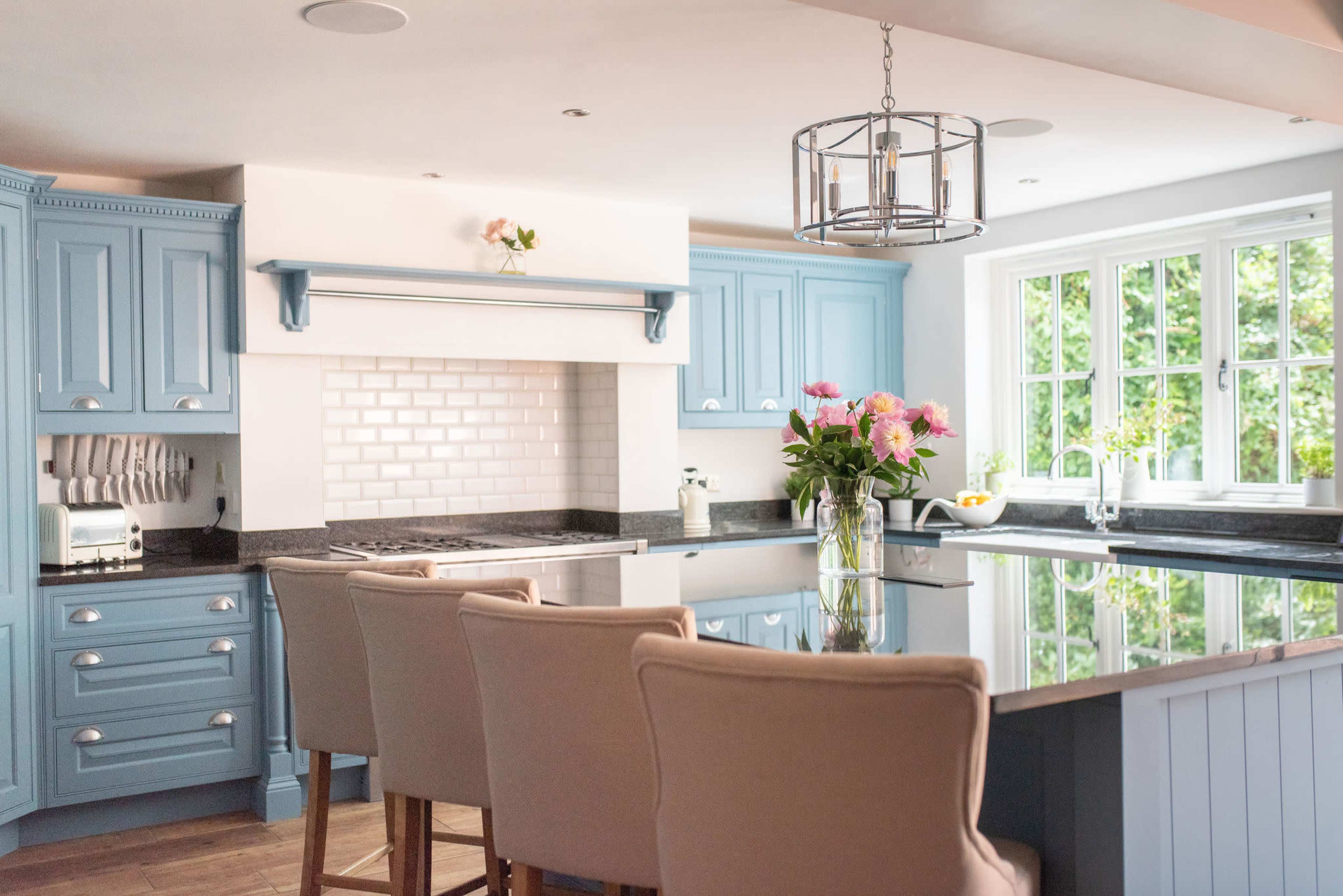 A kitchen with light blue cabinets, a central island with seating, and a bowl of flowers on the counter.