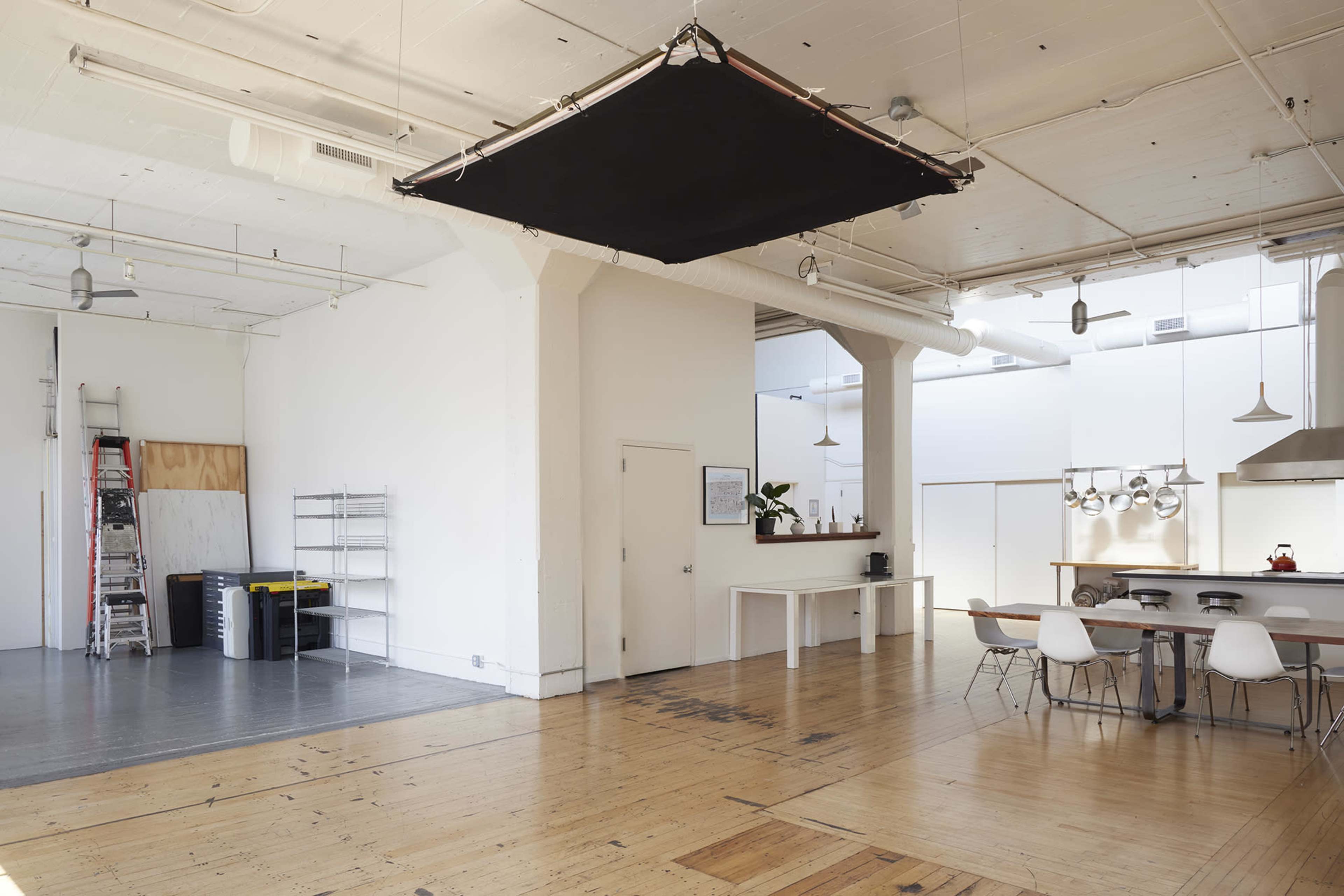 A spacious, minimalist interior with wooden floors, white walls, and a black ceiling panel suspended above a central area featuring a dining table and chairs.