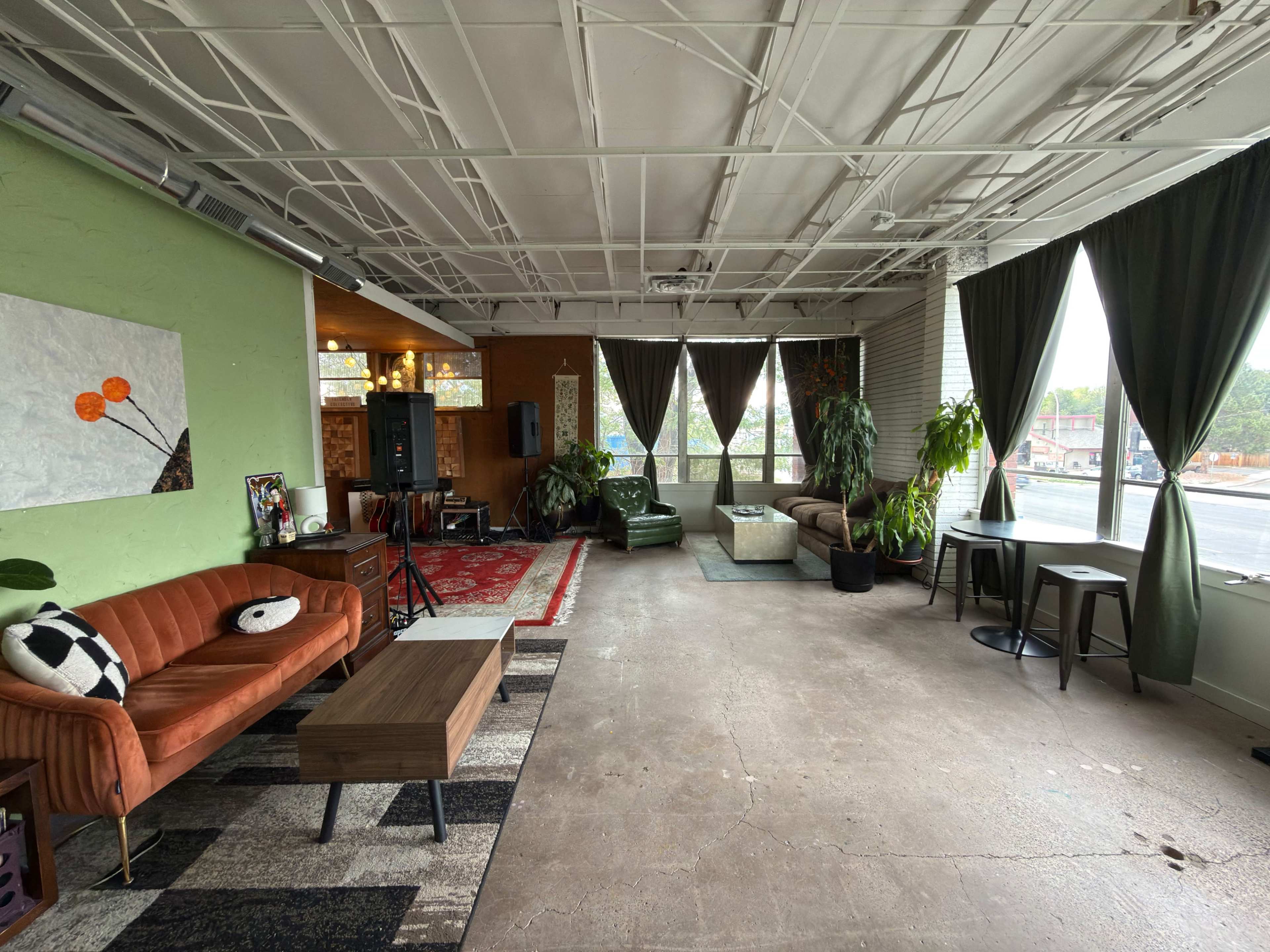 The image shows a spacious, modern lounge area with a mix of seating options, green walls, and large windows allowing natural light to enter.