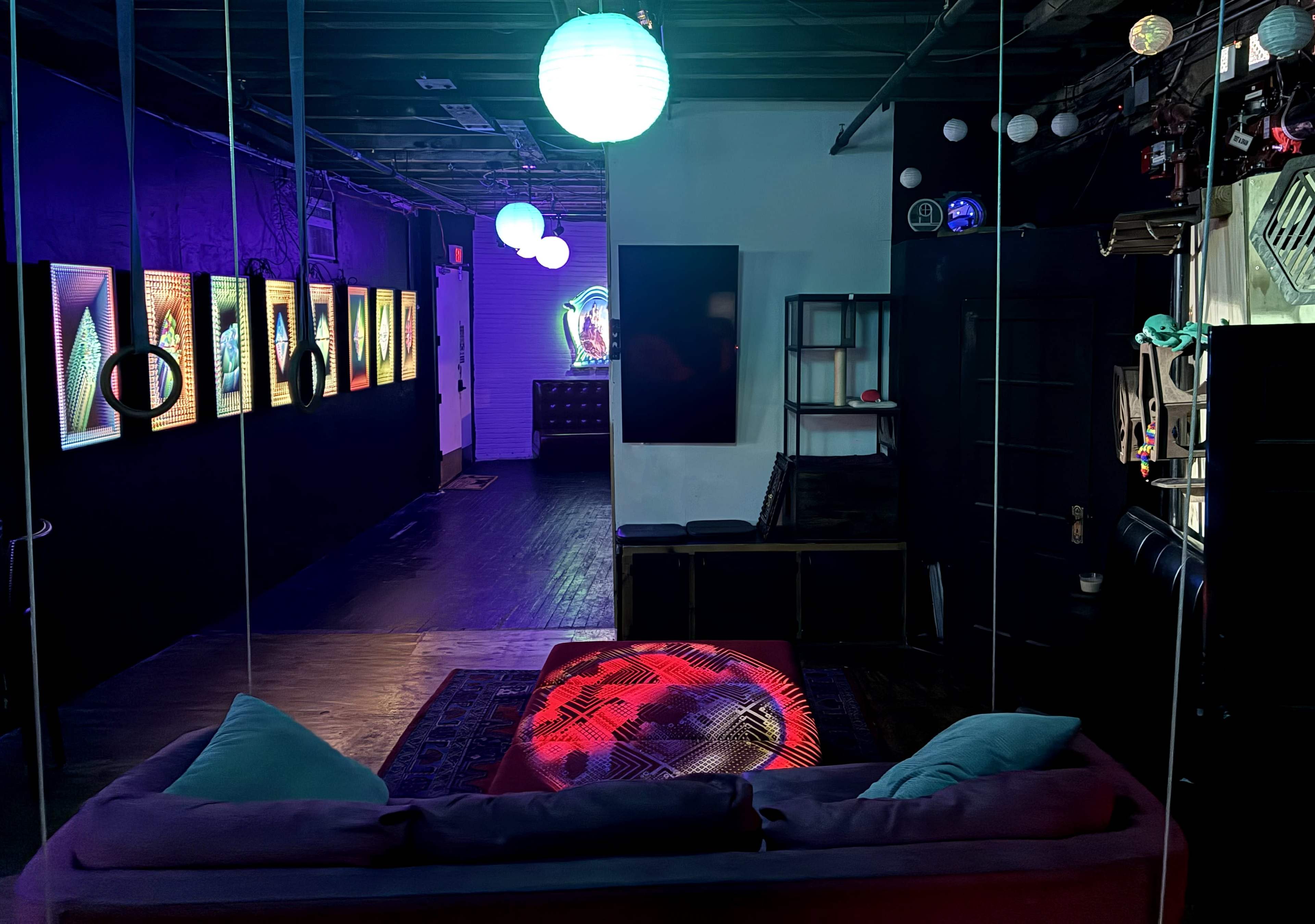 The image shows a modern, dimly lit interior featuring a seating area with a colorful light display and walls adorned with illuminated artwork.