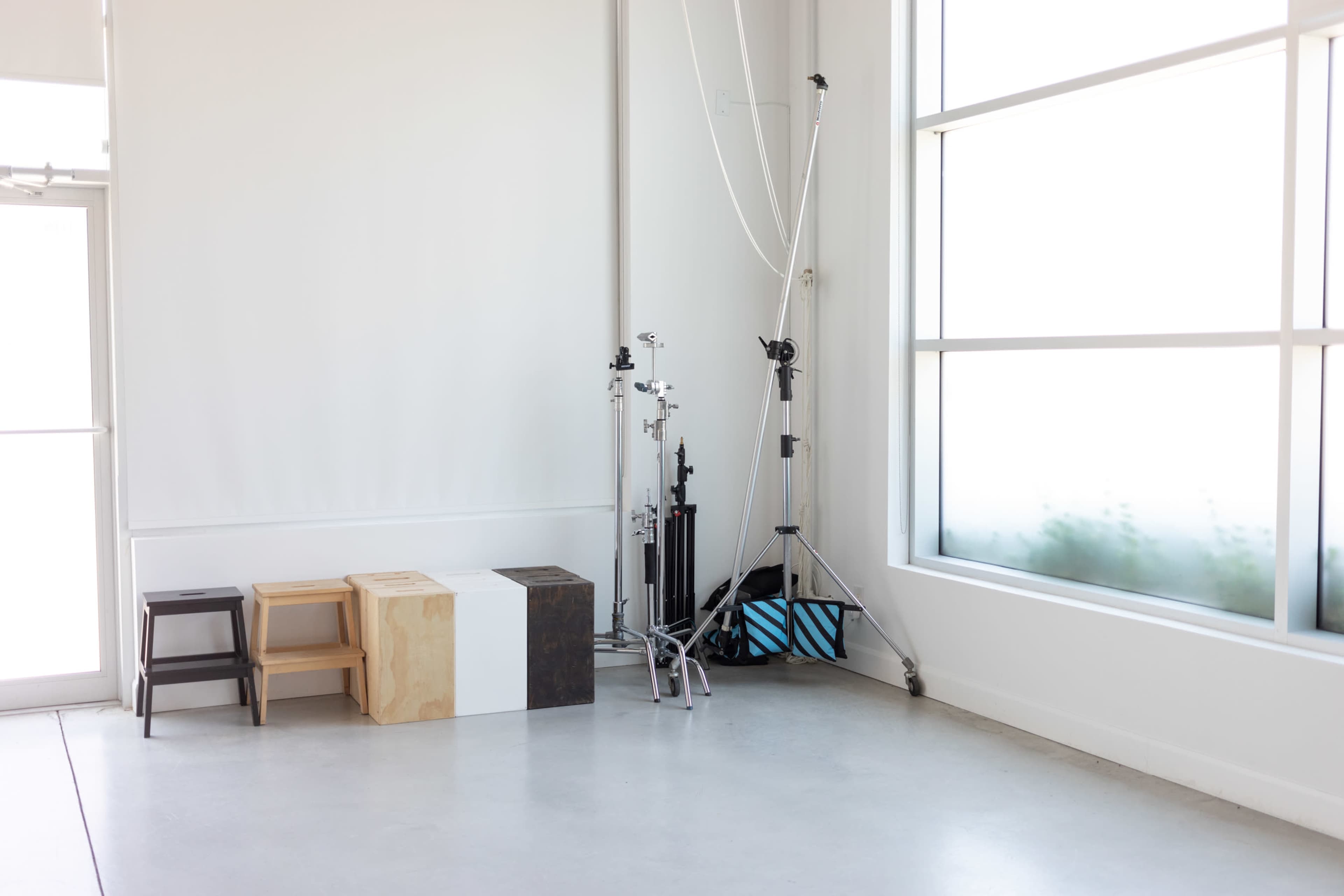 A brightly lit studio corner with three wooden blocks and photography equipment against a white wall.