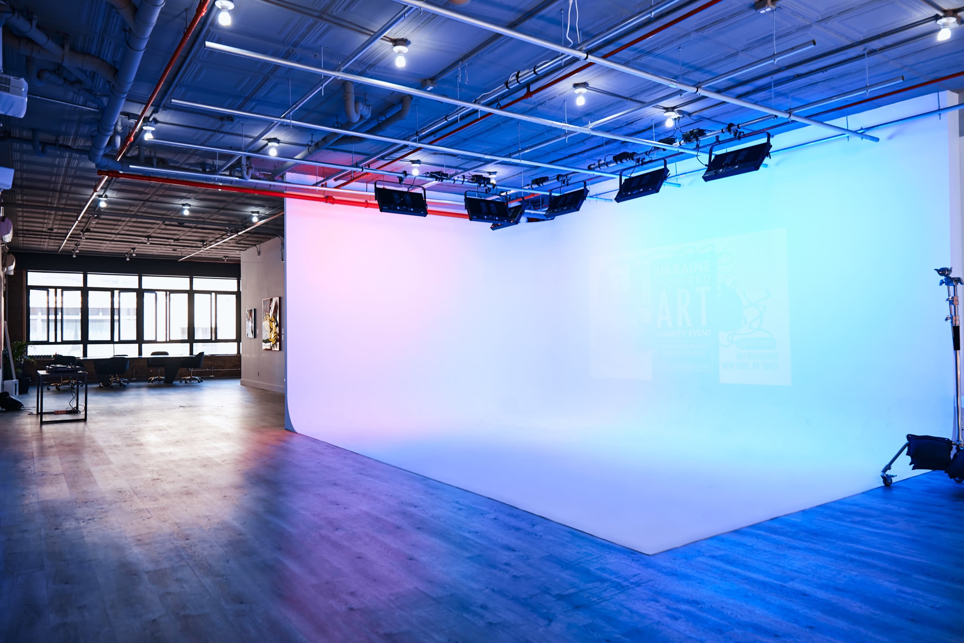 A spacious studio with a seamless white backdrop, illuminated by blue and purple lighting, and equipped with track lighting fixtures.