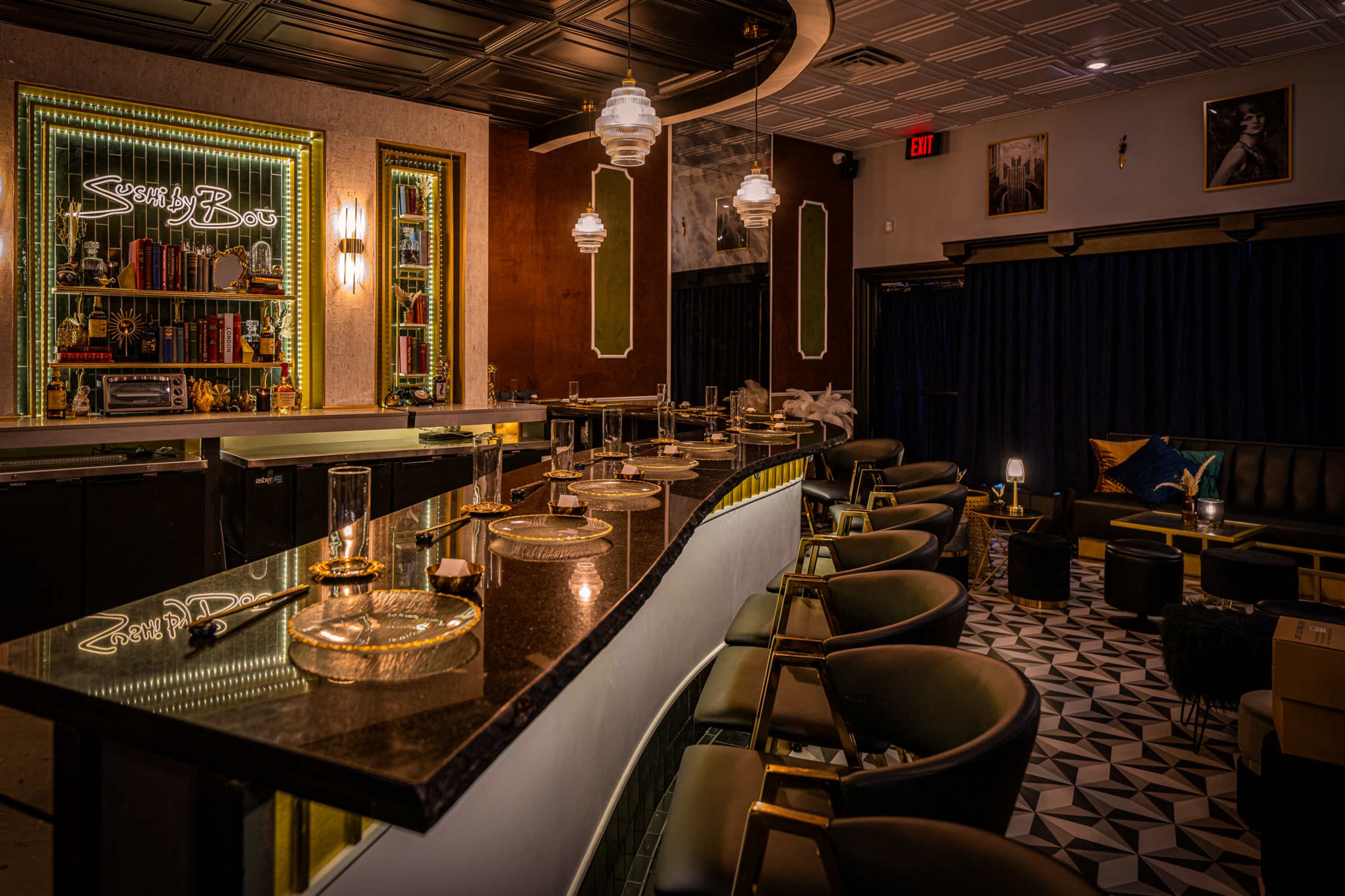 The image shows an elegantly designed bar area featuring a long, black granite counter, stylish seating, and decorative lighting.