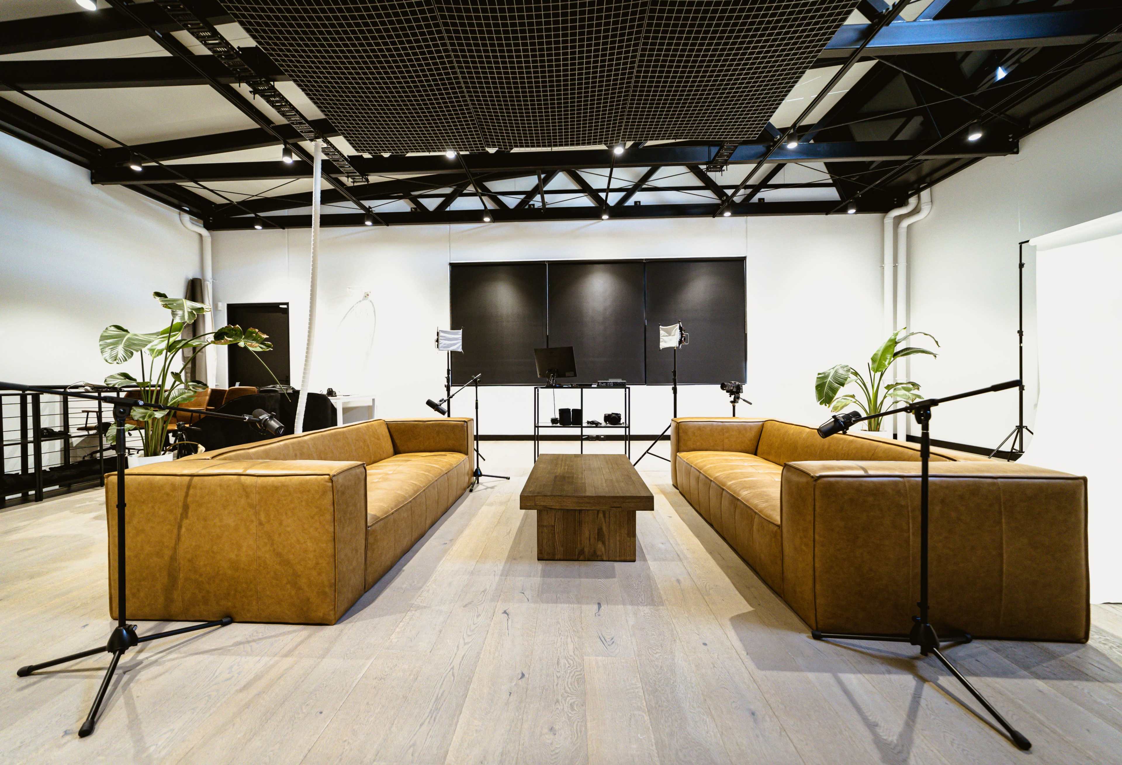 A modern, open space with two brown leather sofas facing each other, a wooden coffee table in the middle, and black wall panels in the background.