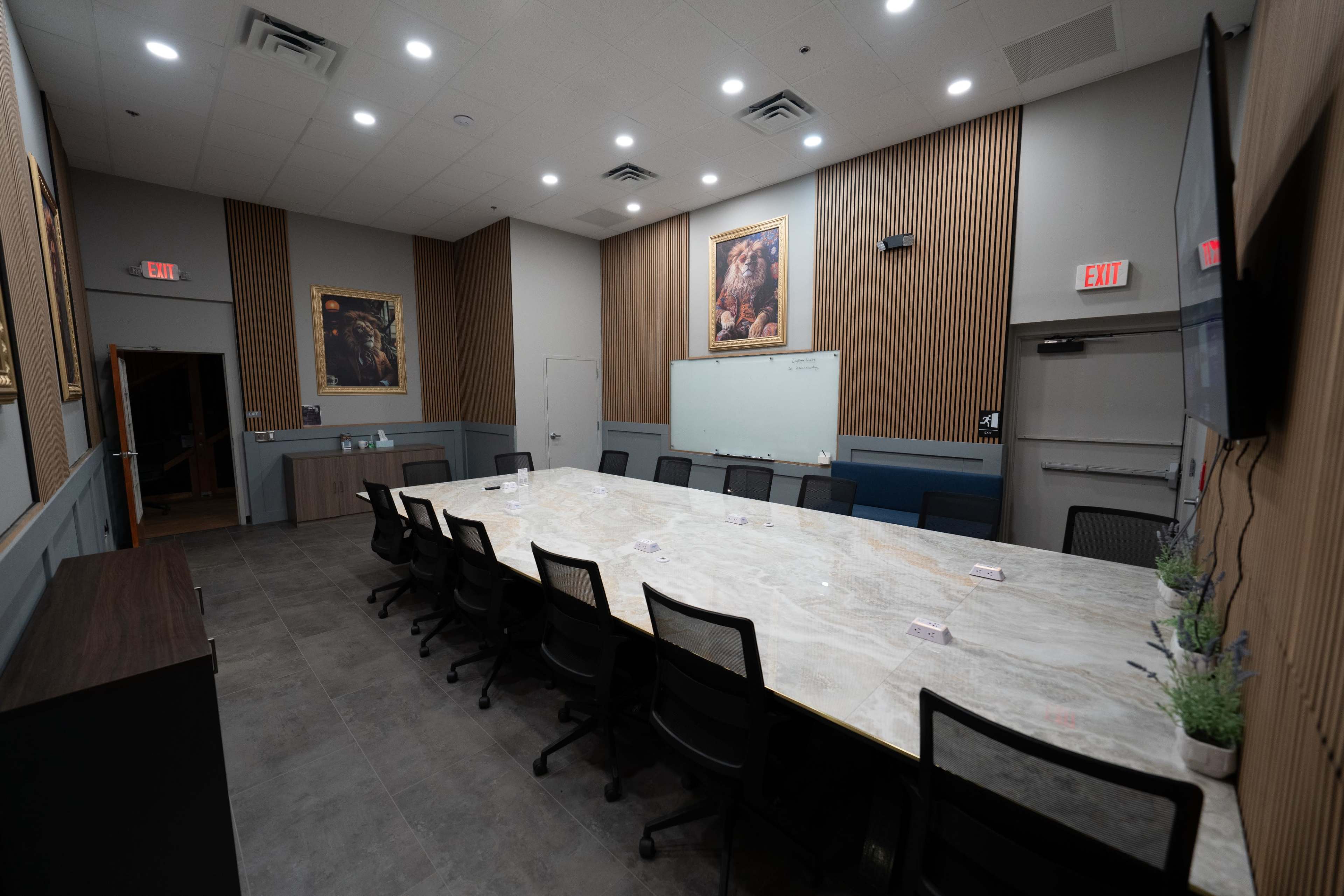 A spacious conference room features a large marble table surrounded by black chairs, with wall art and a whiteboard visible.