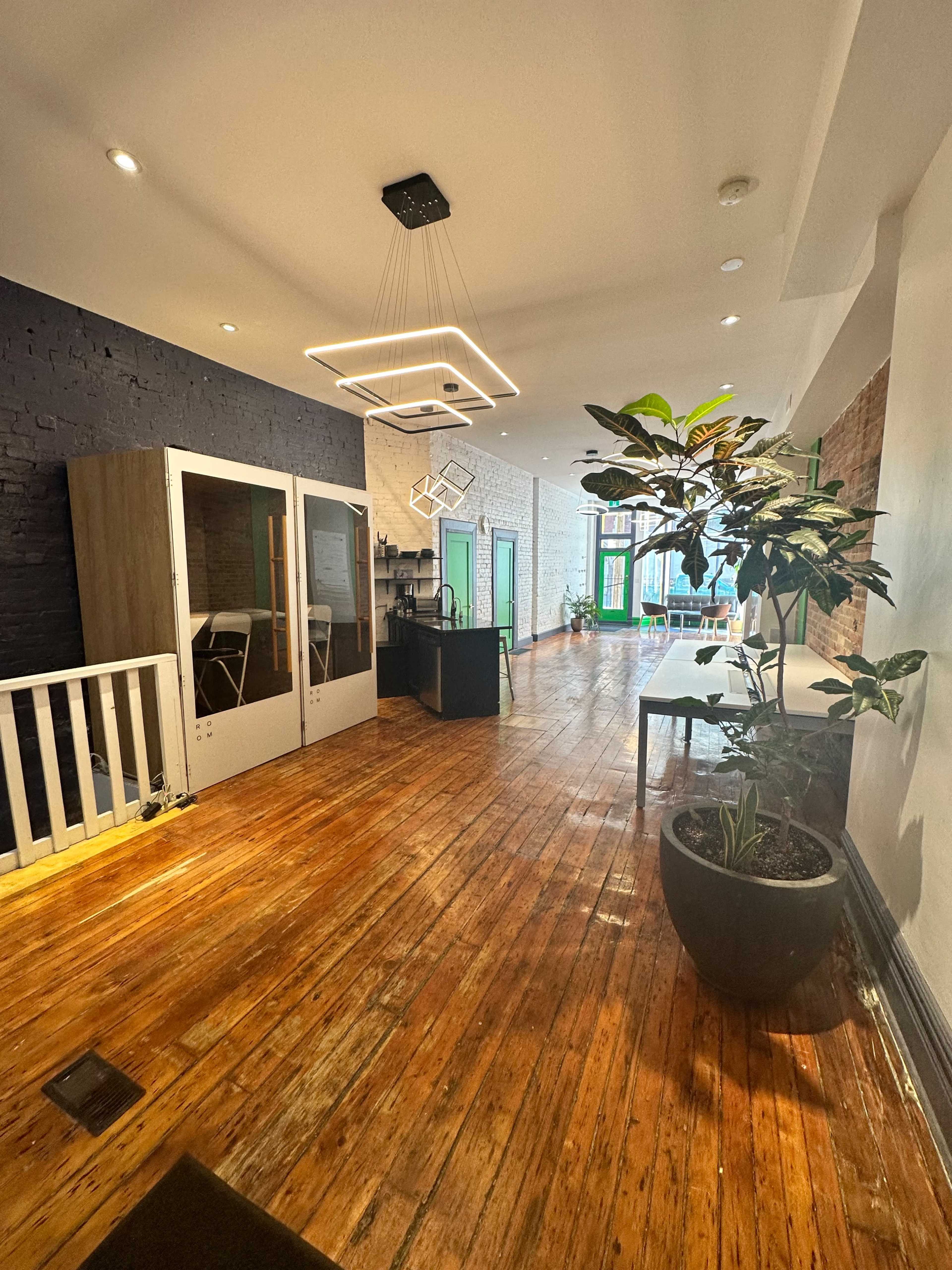 A modern office interior with wooden floors, large windows, and a mix of open and enclosed workspaces.