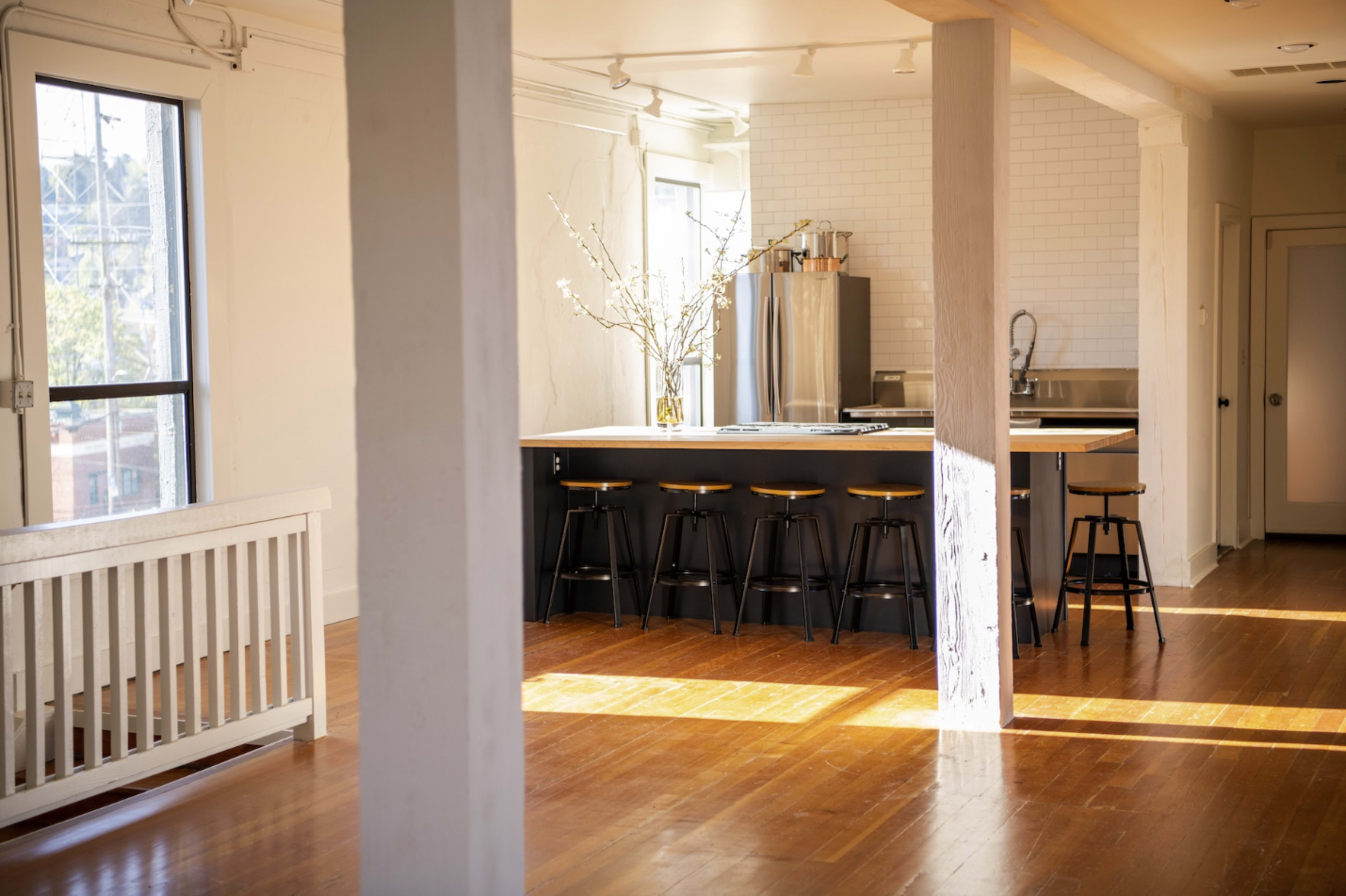 A spacious, modern kitchen with a large island, a line of stools, and natural light streaming through large windows.