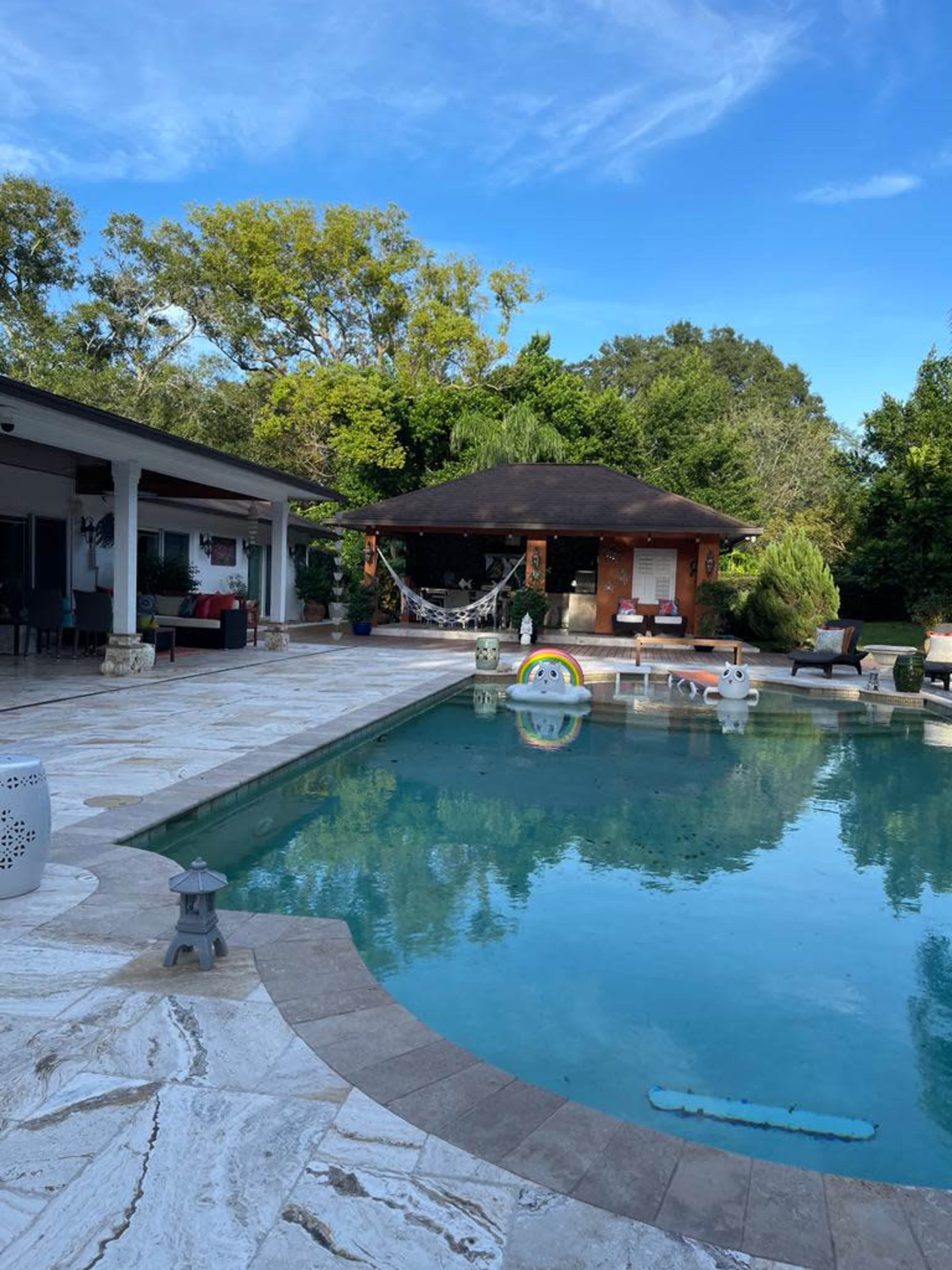 The image shows a residential backyard with a swimming pool surrounded by a patio and a gazebo in the background.