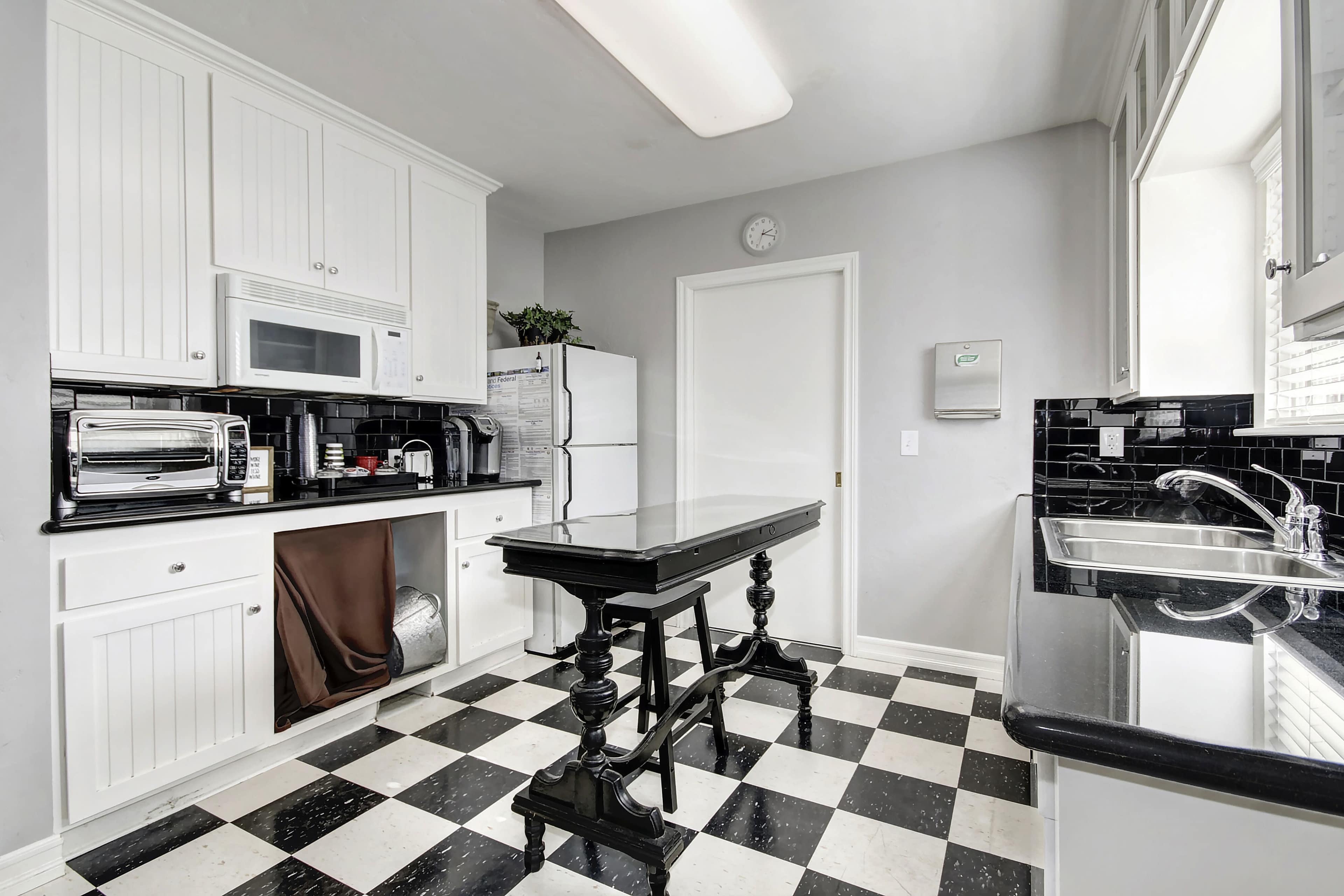 A modern kitchen with white cabinetry, a black and white checkered floor, and a central island.
