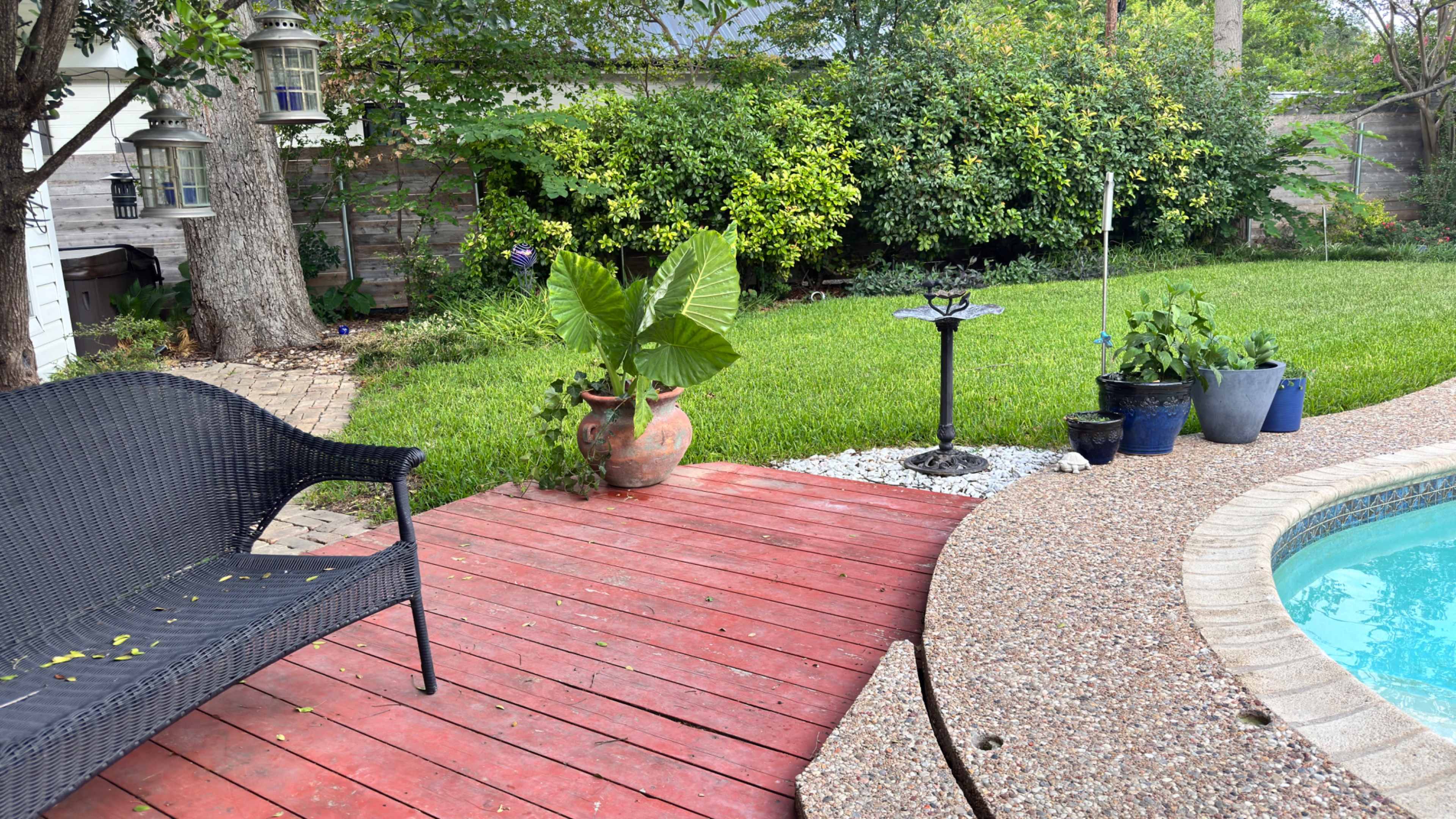The image shows a backyard scene featuring a wooden deck leading to a round pool, surrounded by greenery and potted plants.