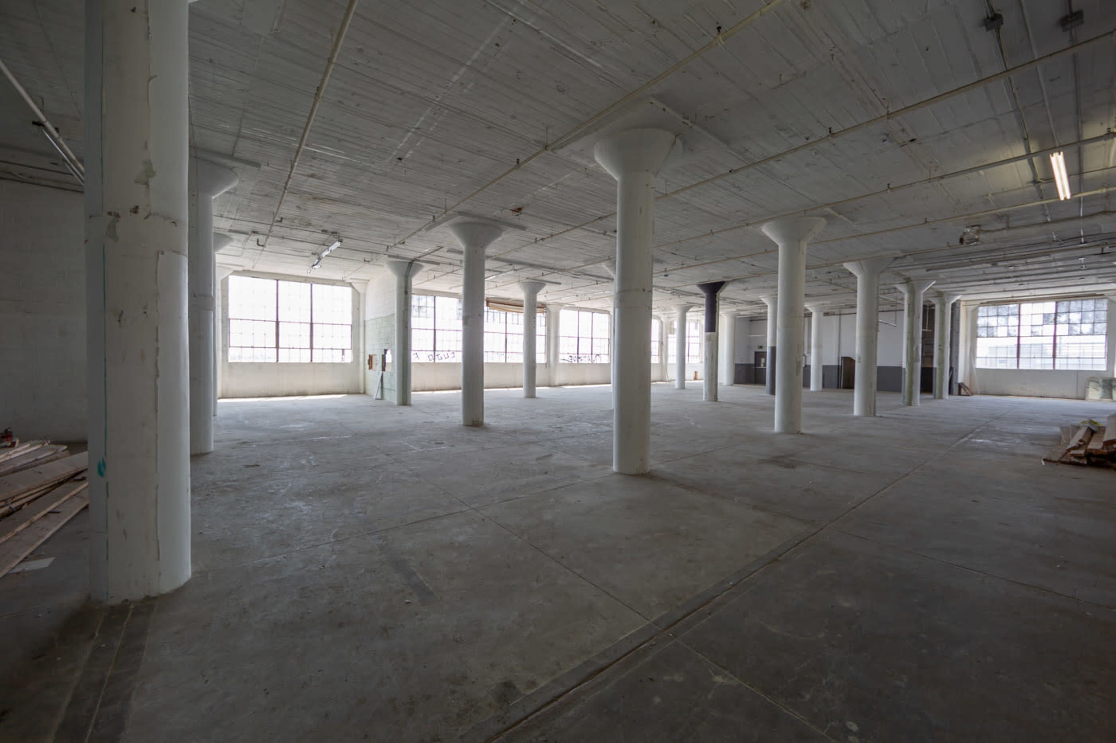 An empty industrial space with large windows and exposed concrete pillars.